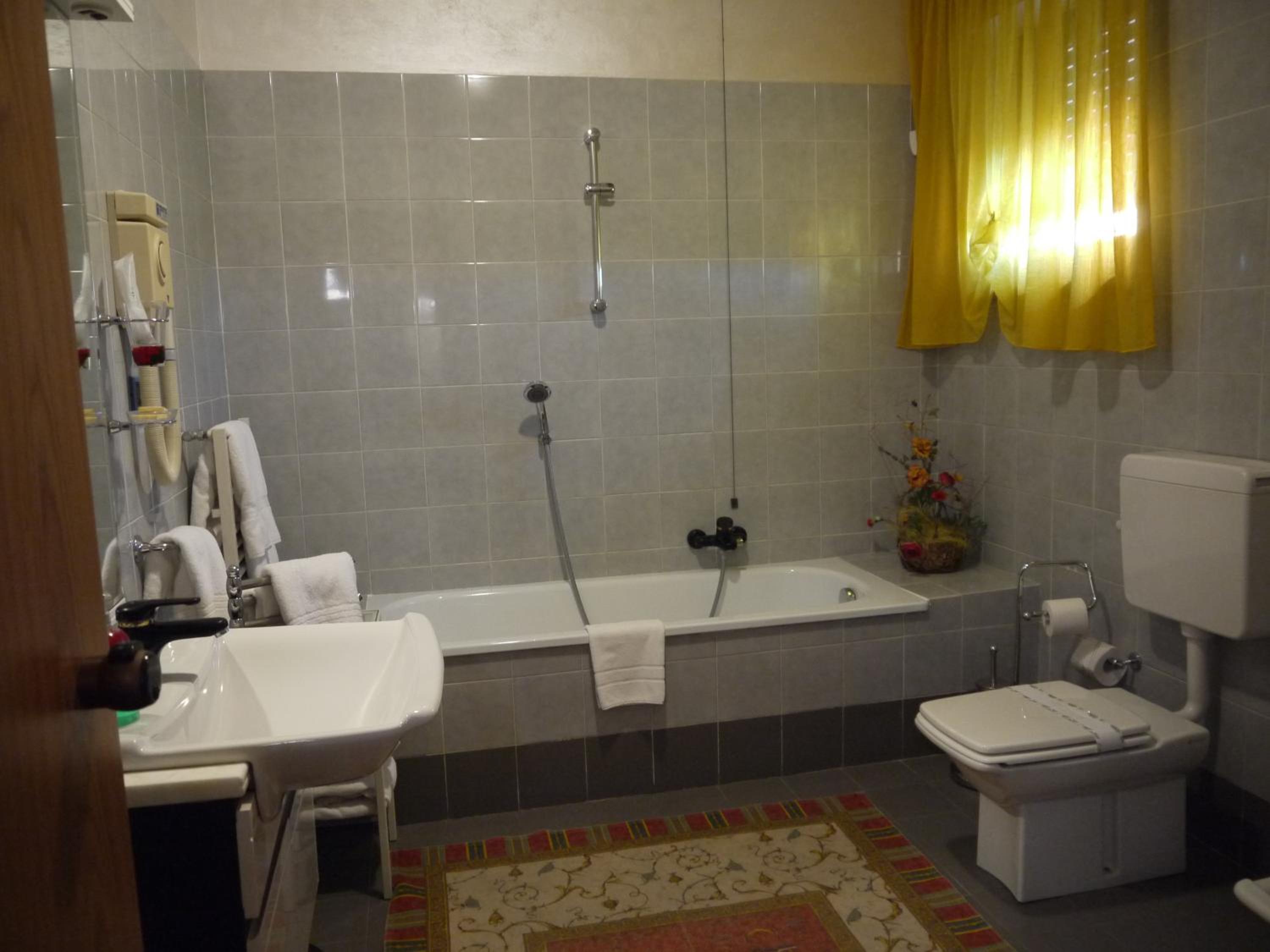 Tiled bathroom with a bathtub, shower head, white sink, toilet, and yellow curtains by the window.