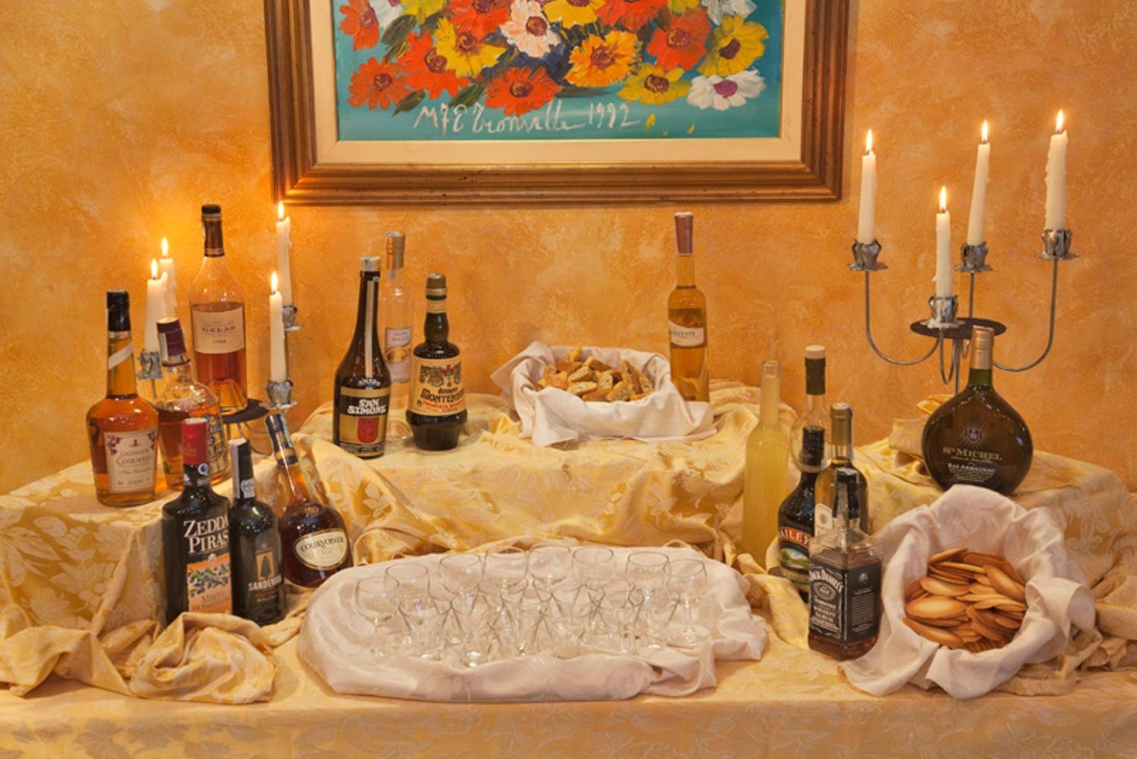 Table spread with liquor bottles, small tasting glasses, baskets of biscuits, and tall burning candles.