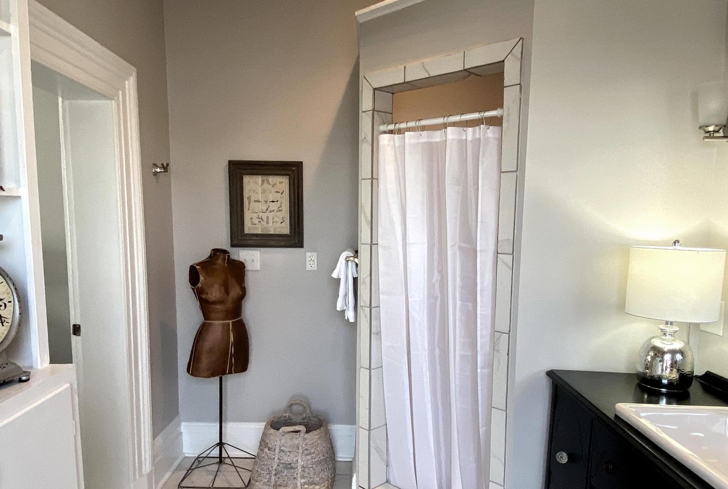 A bathroom featuring a marble-framed shower stall, a vintage dress form, and a vanity lamp.