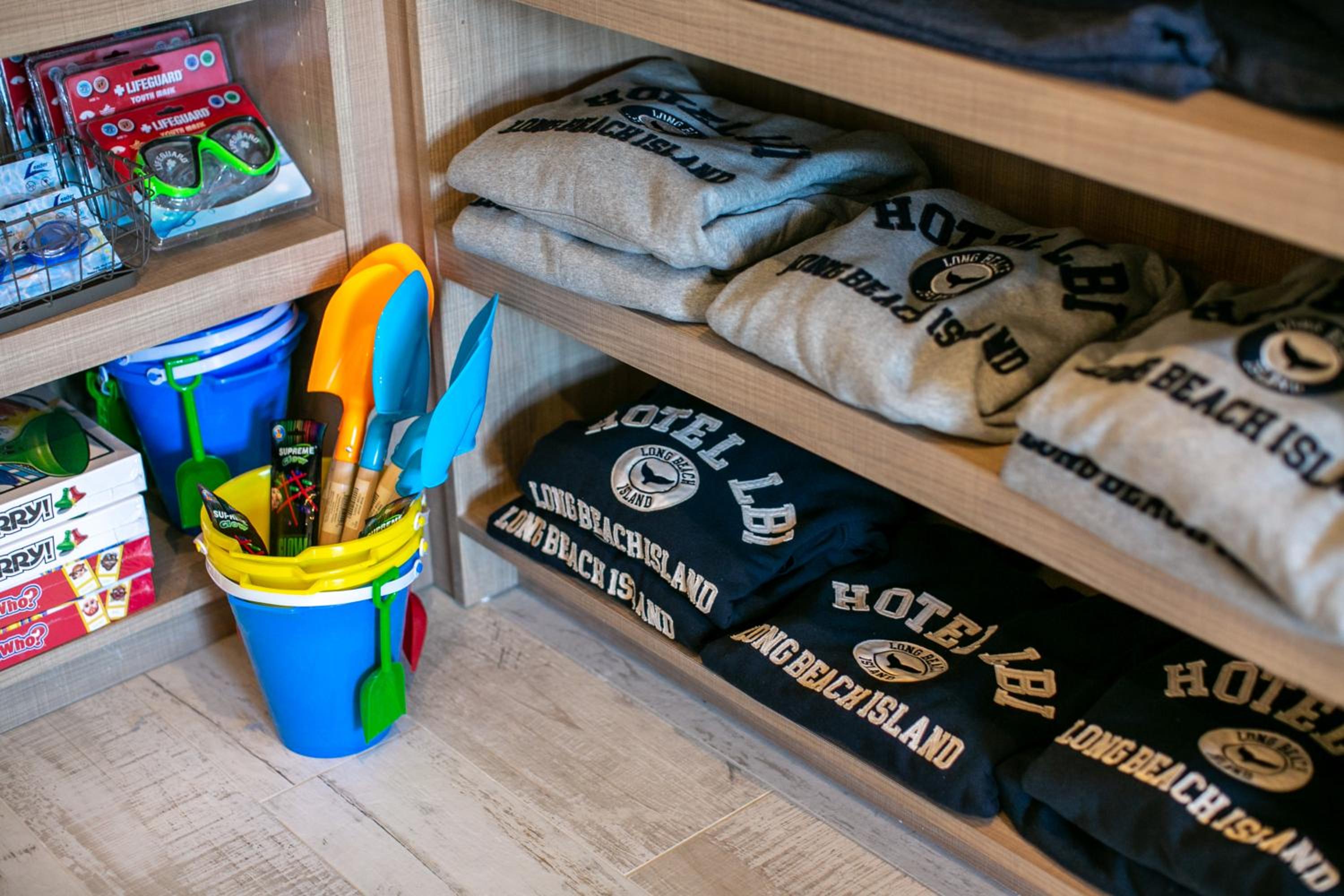 Wooden gift shop shelves with folded sweatshirts, colorful sand buckets, and toy shovels.