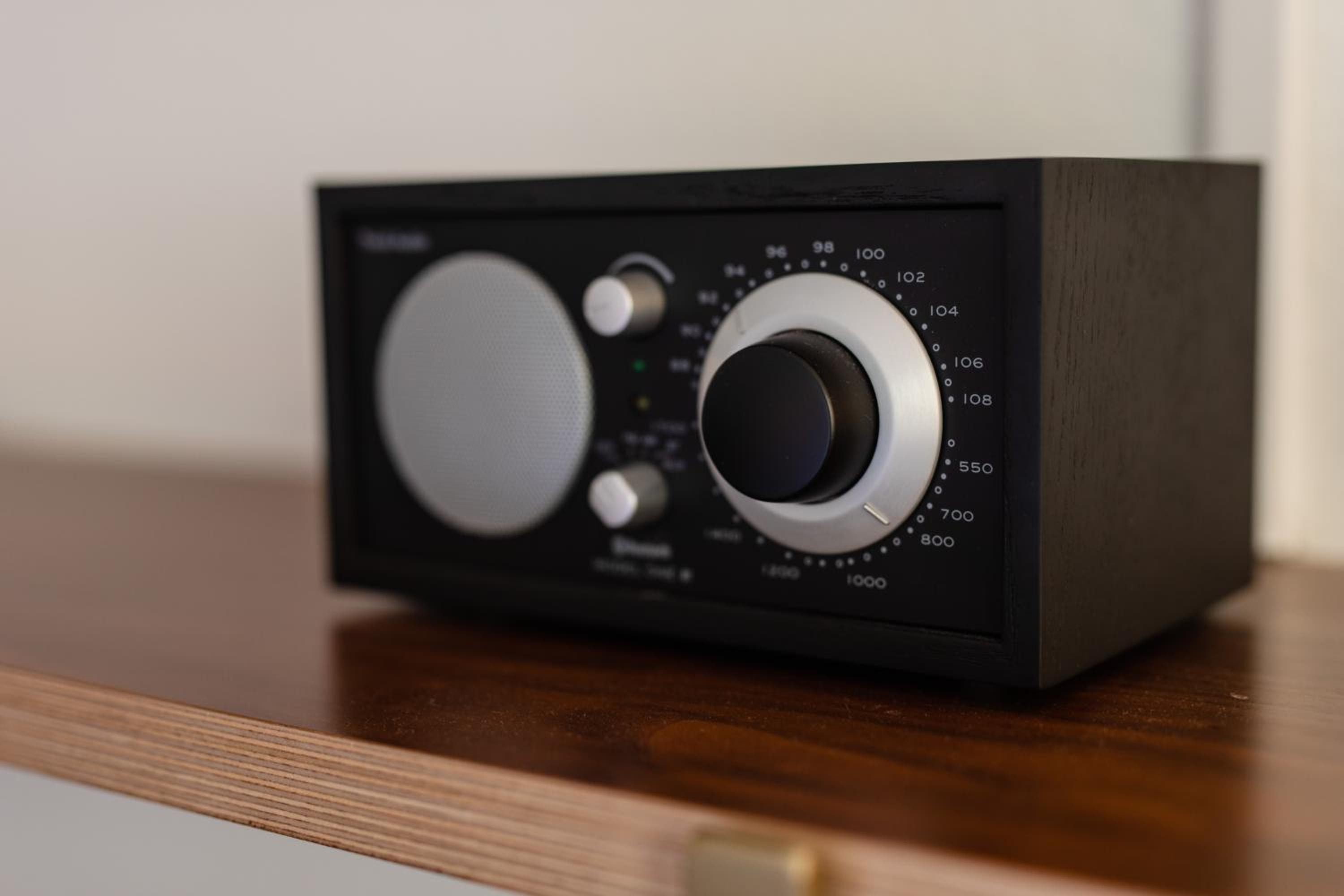 A black radio sits on a wooden shelf in soft indoor light.