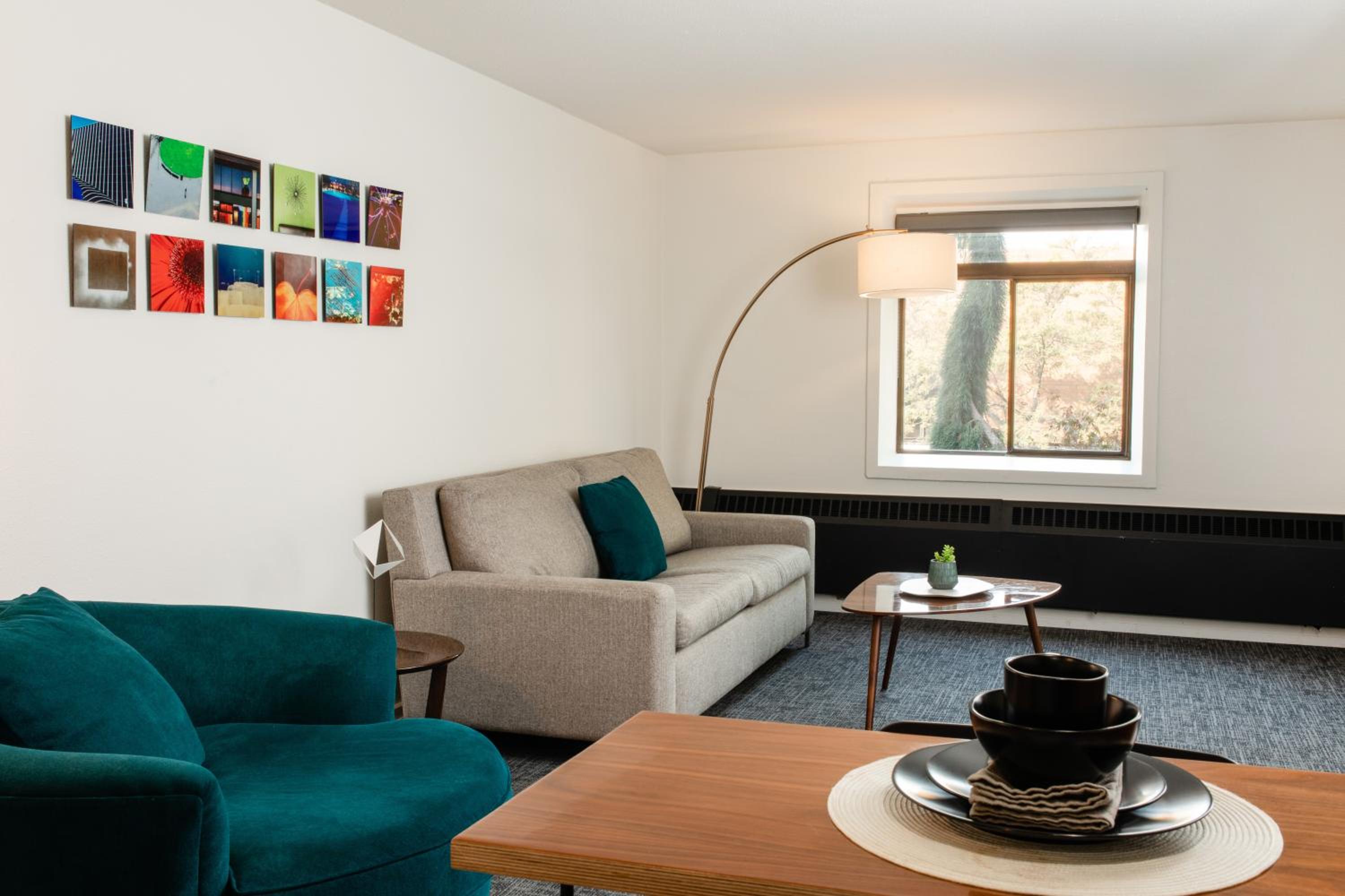 A living room features a grey sofa, teal armchair, and curved floor lamp near a window.