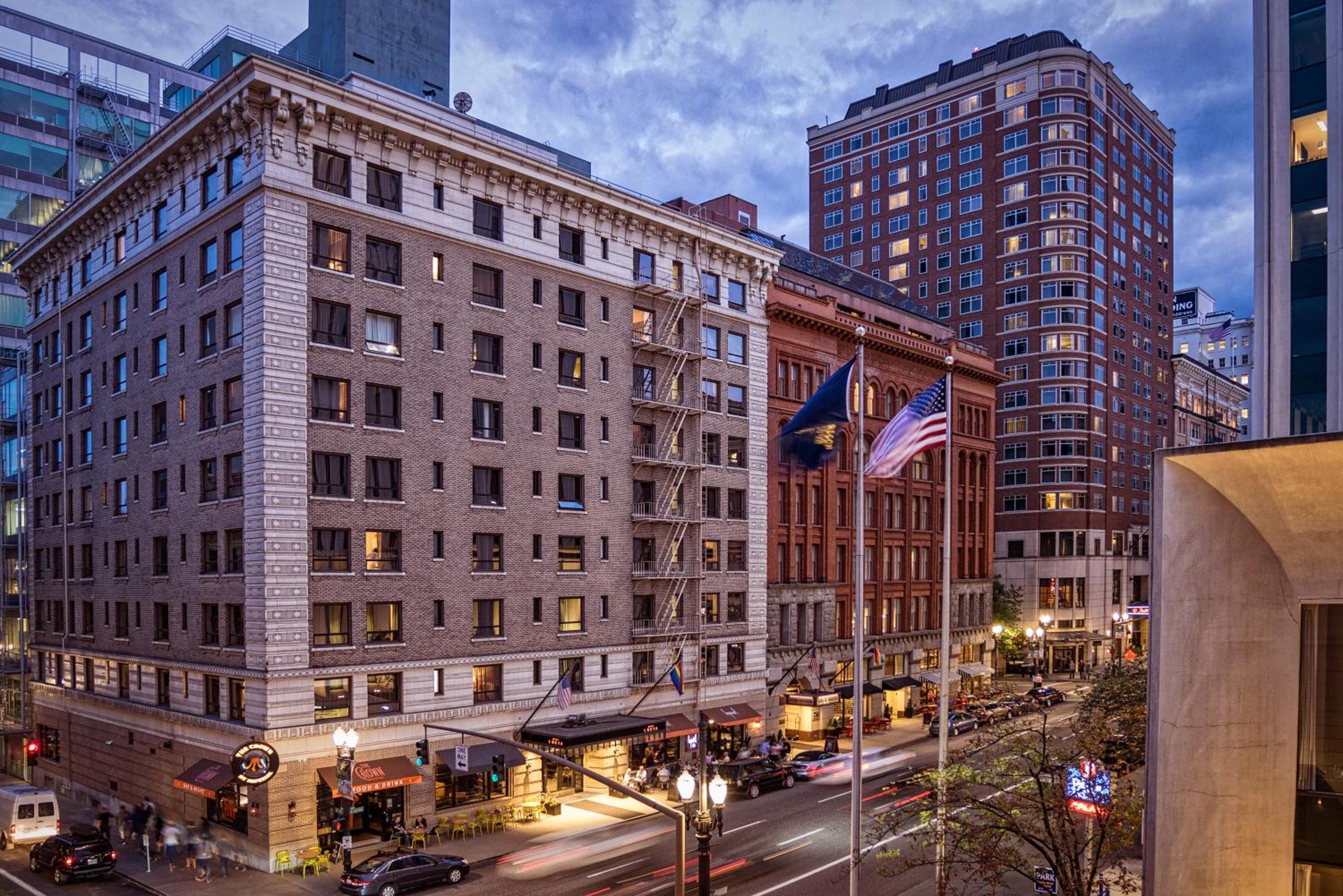 Exterior view of Hotel Lucia's brick facade at dusk with streetlights and passing traffic below.