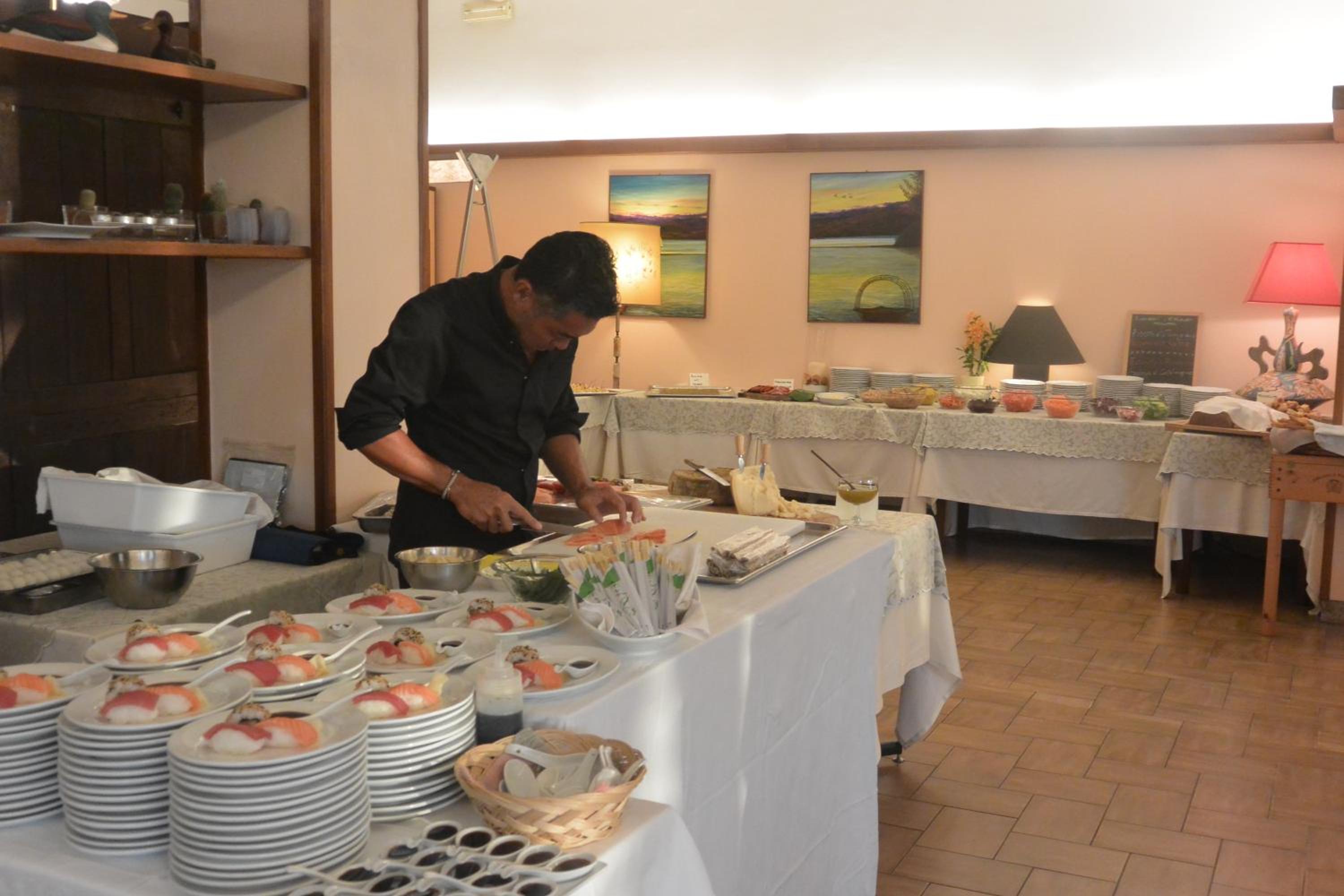 Chef slices fish at a buffet table laden with plates of prepared sushi and food displays.