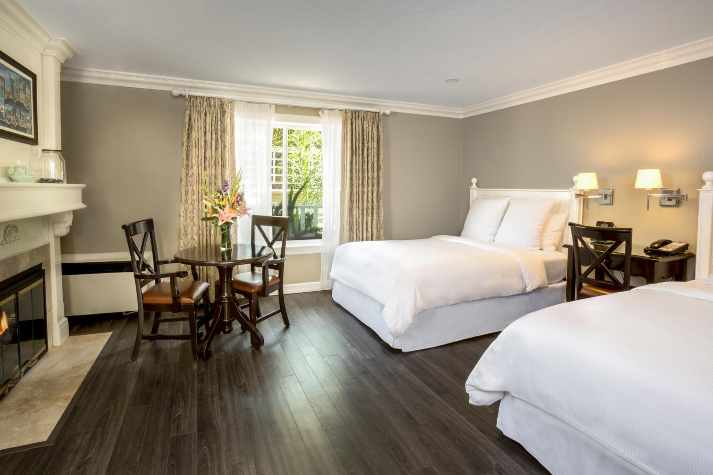 Guest room with dark wood flooring, white-dressed beds, a fireplace, and dining table.