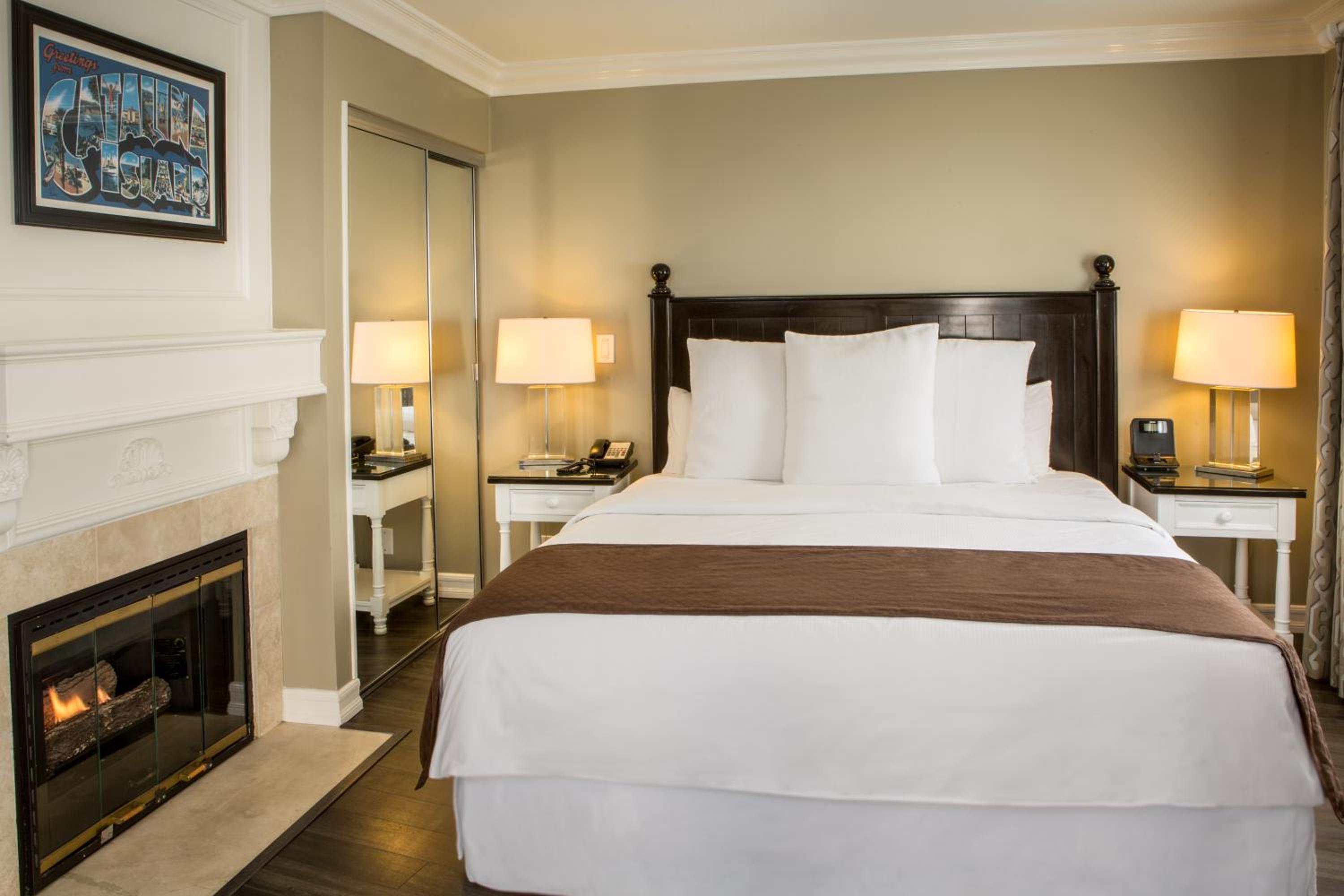 Guest bedroom with dark wood headboard, white linens, bedside lamps, and a lit fireplace.