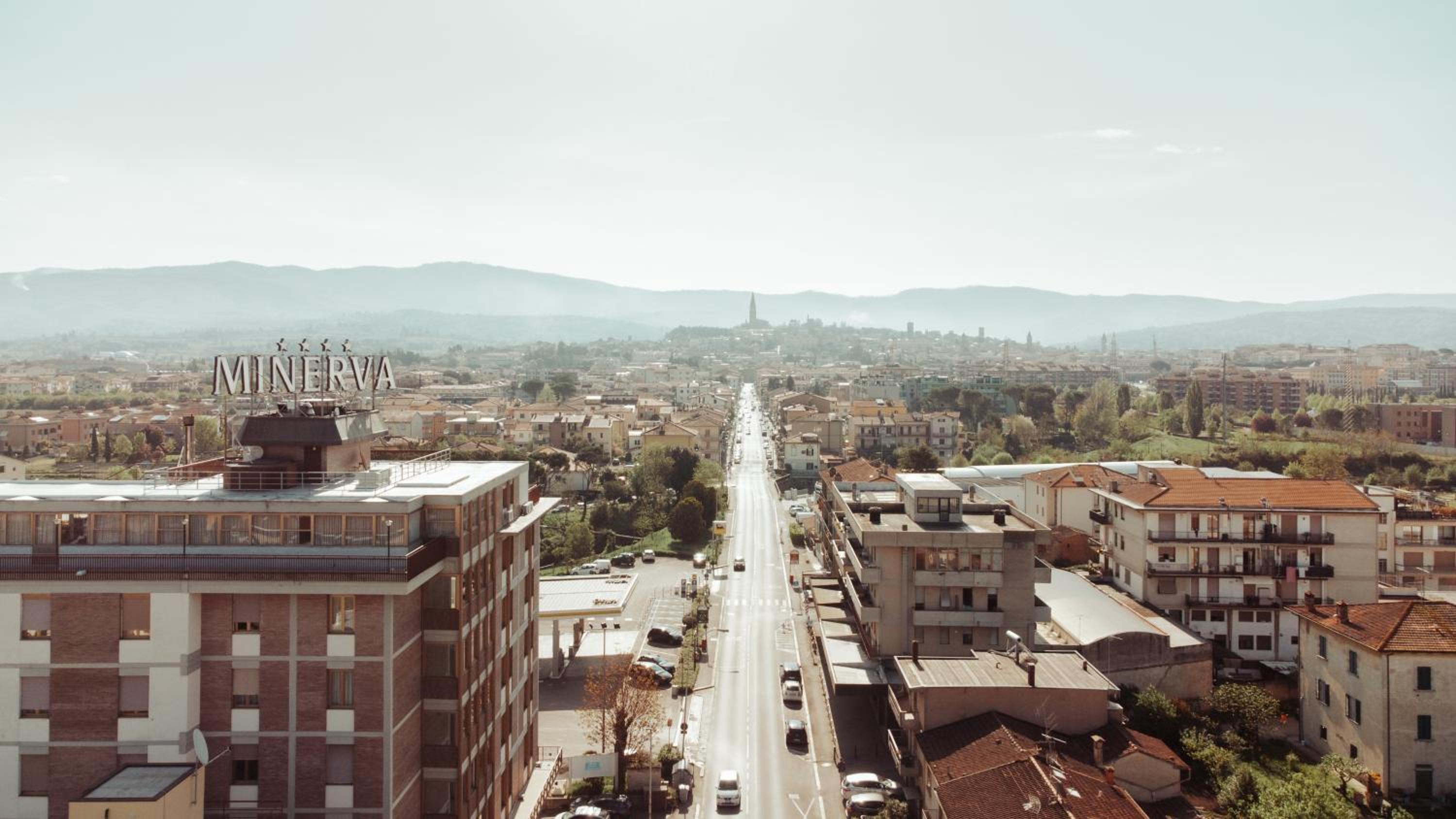 High-angle view along a straight road toward the historic town and distant hills, with the Minerva rooftop sign.