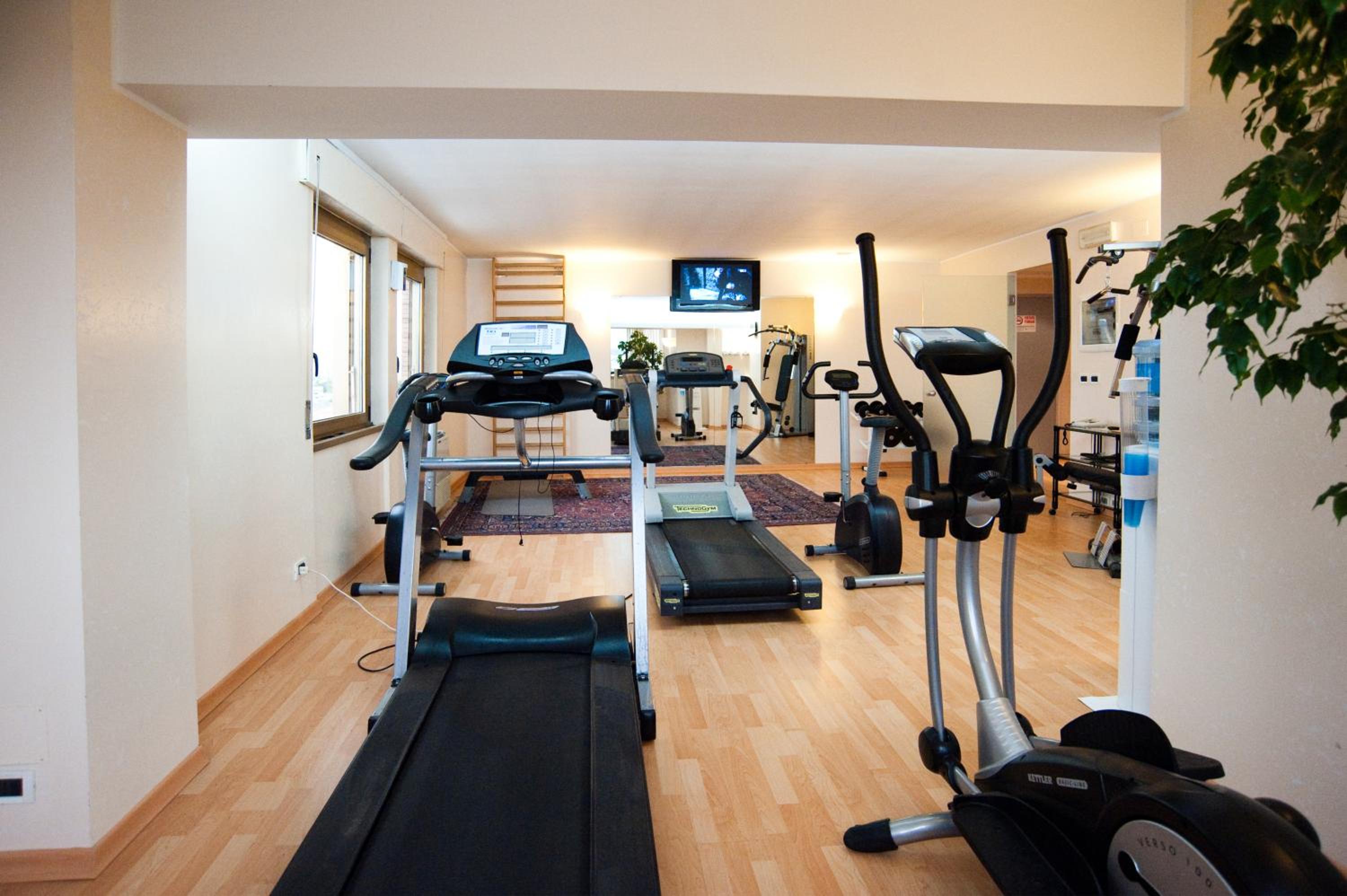 Hotel fitness center with treadmills, stationary bikes, and an elliptical machine on wood-laminate flooring.