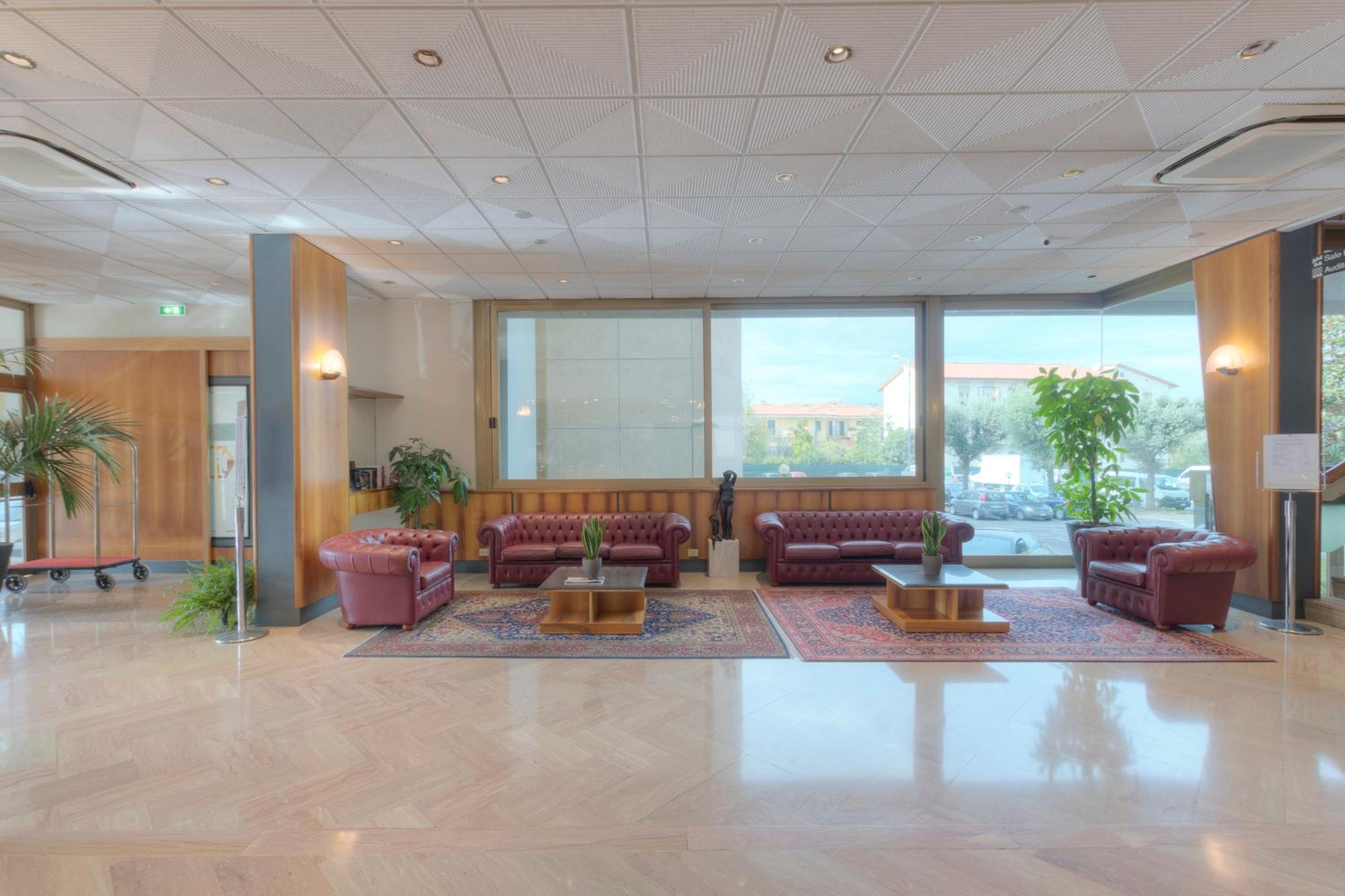 Hotel lobby with polished stone floors, tufted leather sofas on patterned rugs, and large exterior windows.