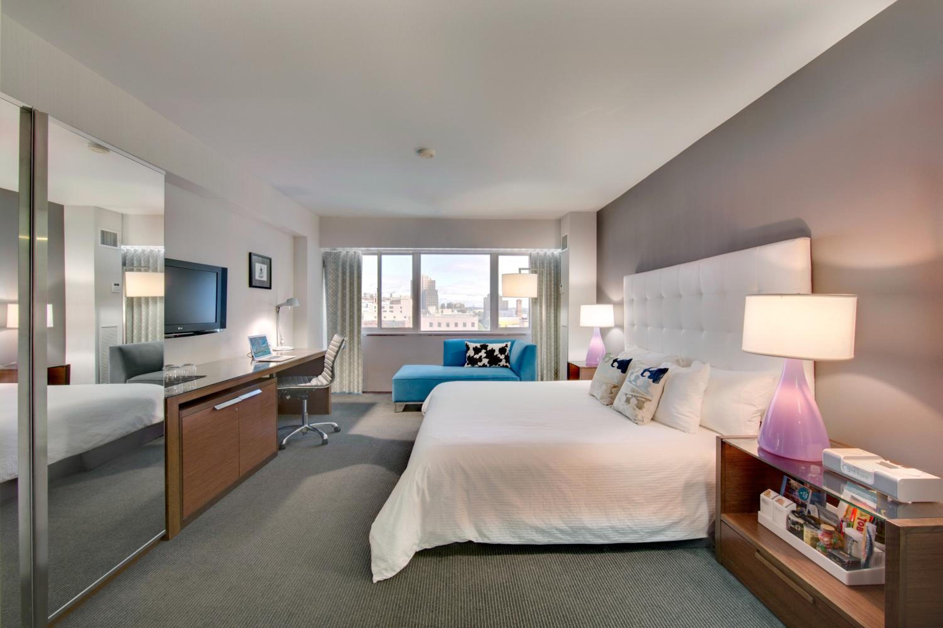 A bedroom with a white tufted headboard, purple bedside lamps, work desk, and a large window.