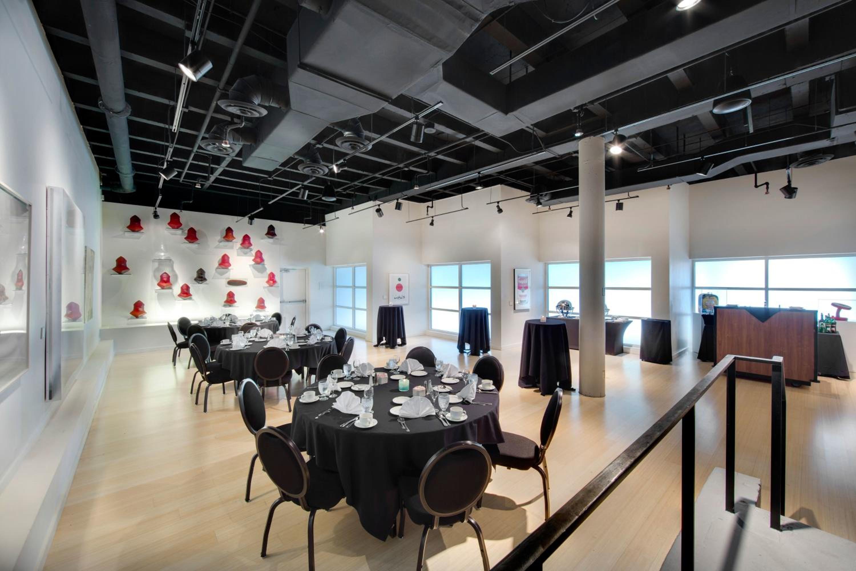 An event hall with black-clothed dining tables, red wall sculptures, and an exposed ceiling.