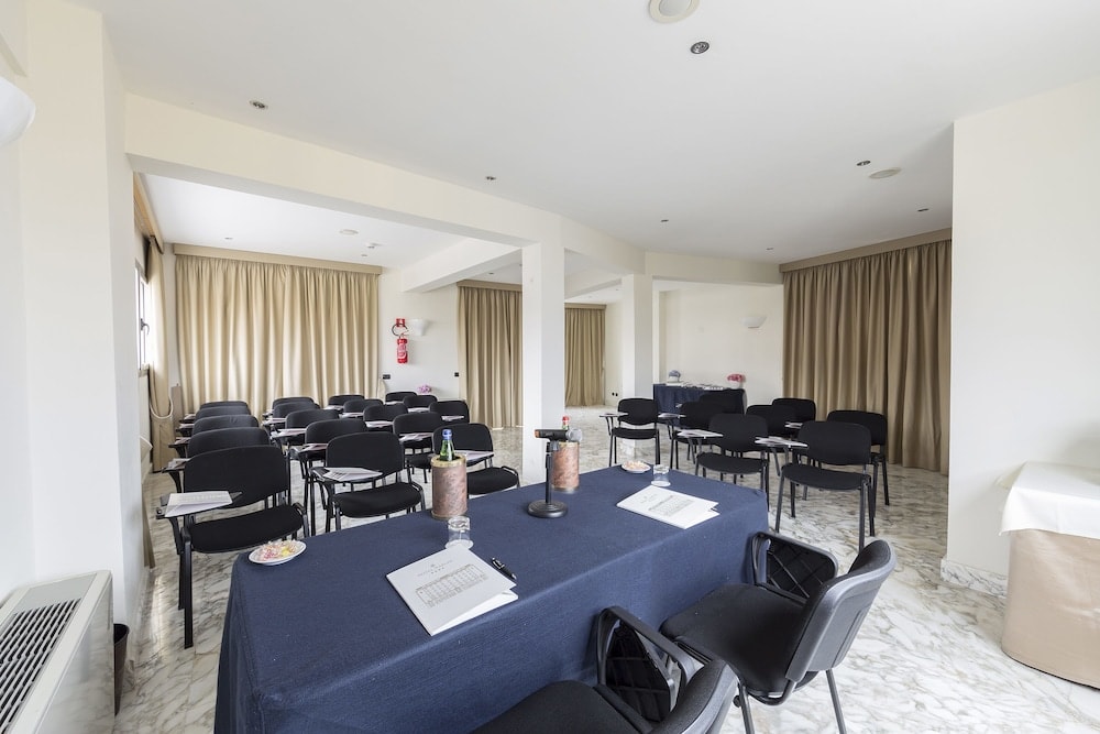 Meeting room with marble floors, rows of black chairs, and a draped presenter table.