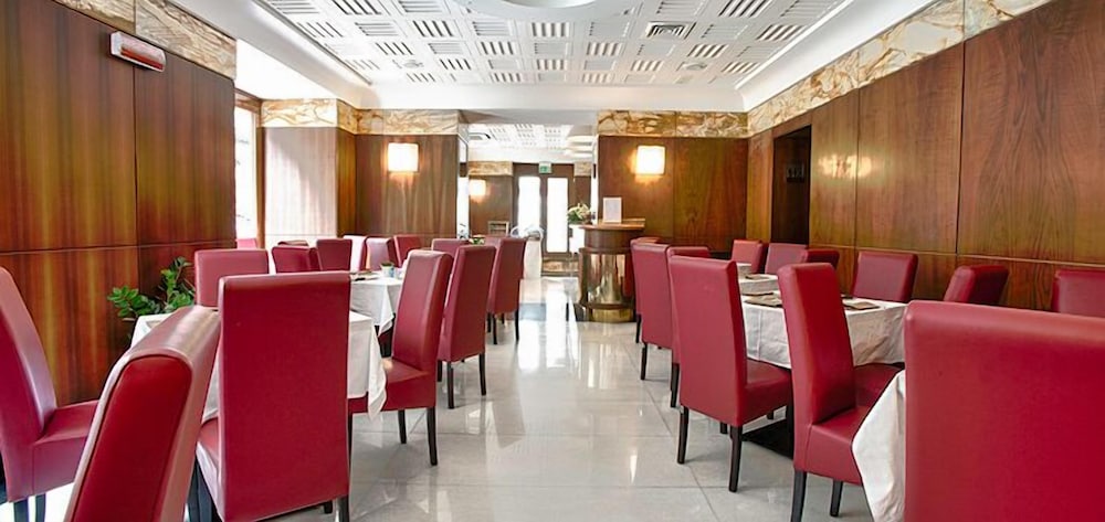 Restaurant dining room with wood-paneled walls, marble flooring, and tables set with red chairs.
