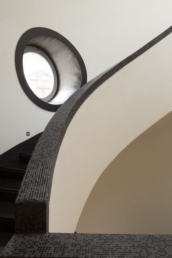 Curved staircase bordered in dark mosaic tile beside a round interior window.