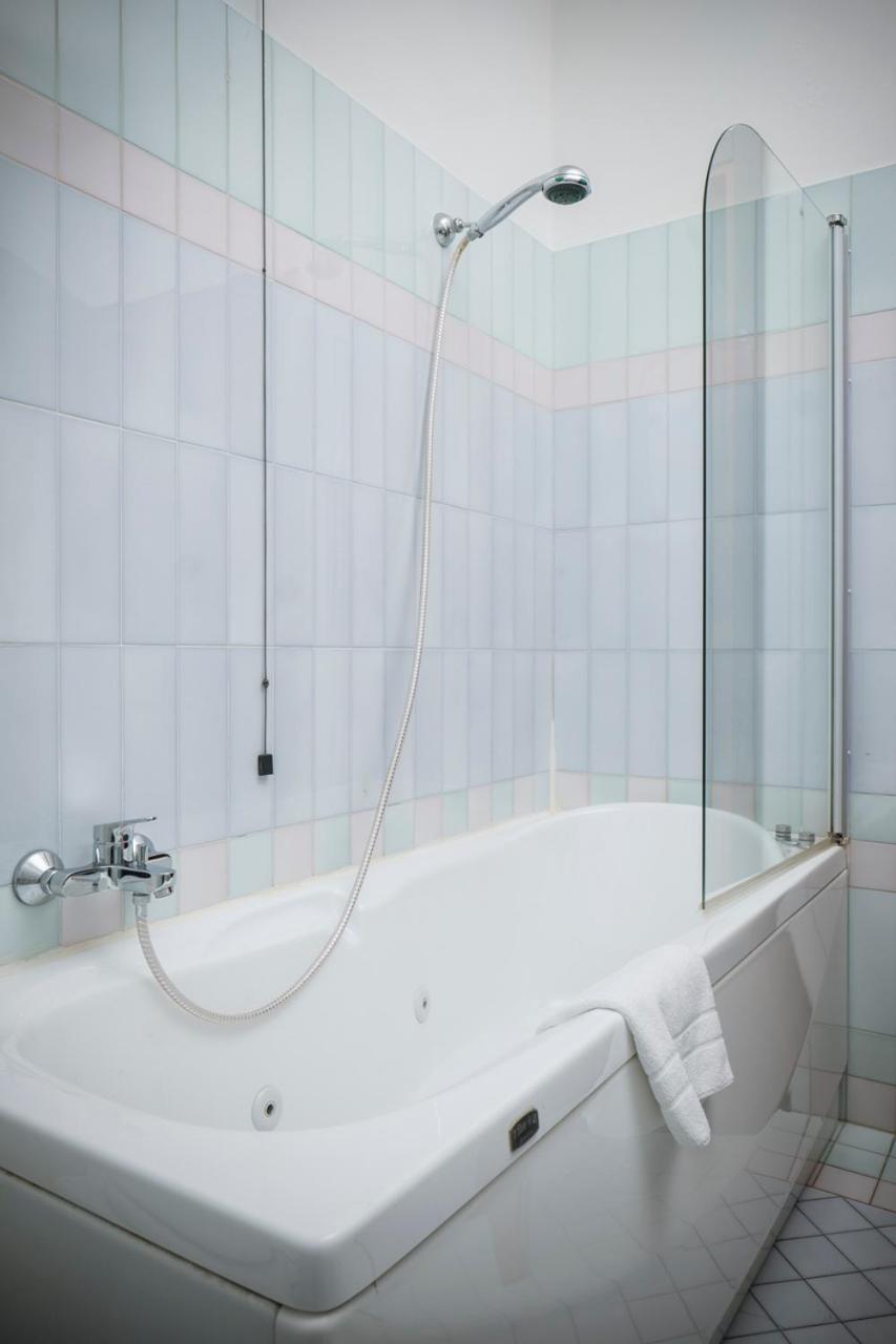 White whirlpool bathtub with a handheld shower attachment beside light pastel tiled walls.