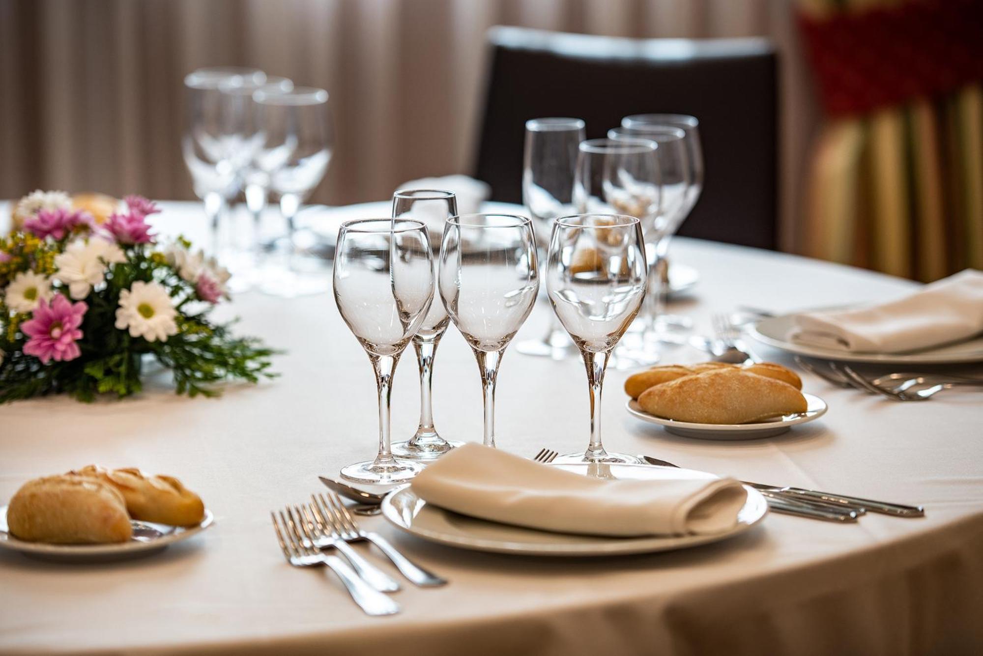 A round banquet table set with white linens, wine glasses, bread plates, and a floral centerpiece.