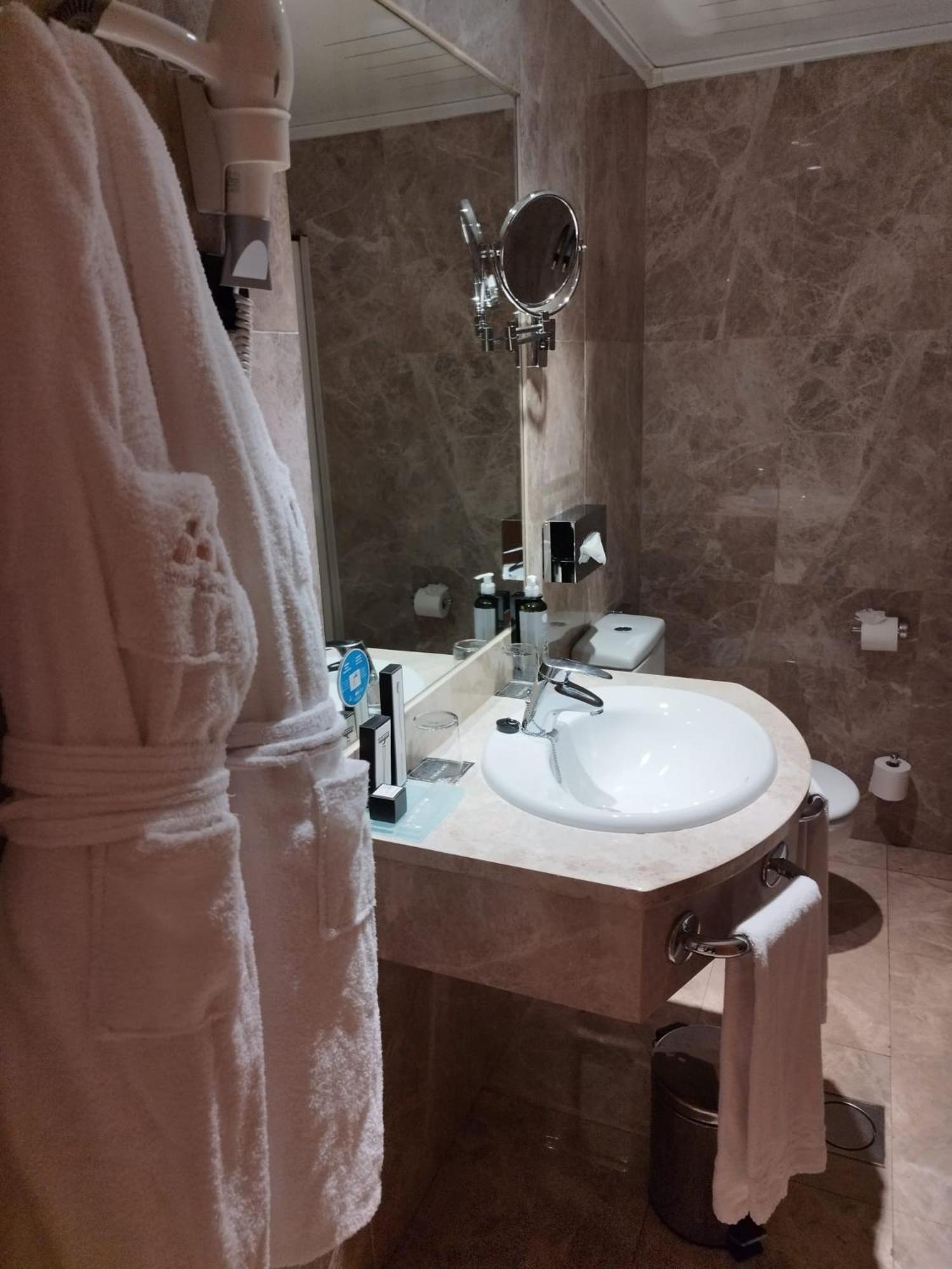 A marble bathroom with a hanging bathrobe in the foreground, a stone vanity, and a wall mirror.