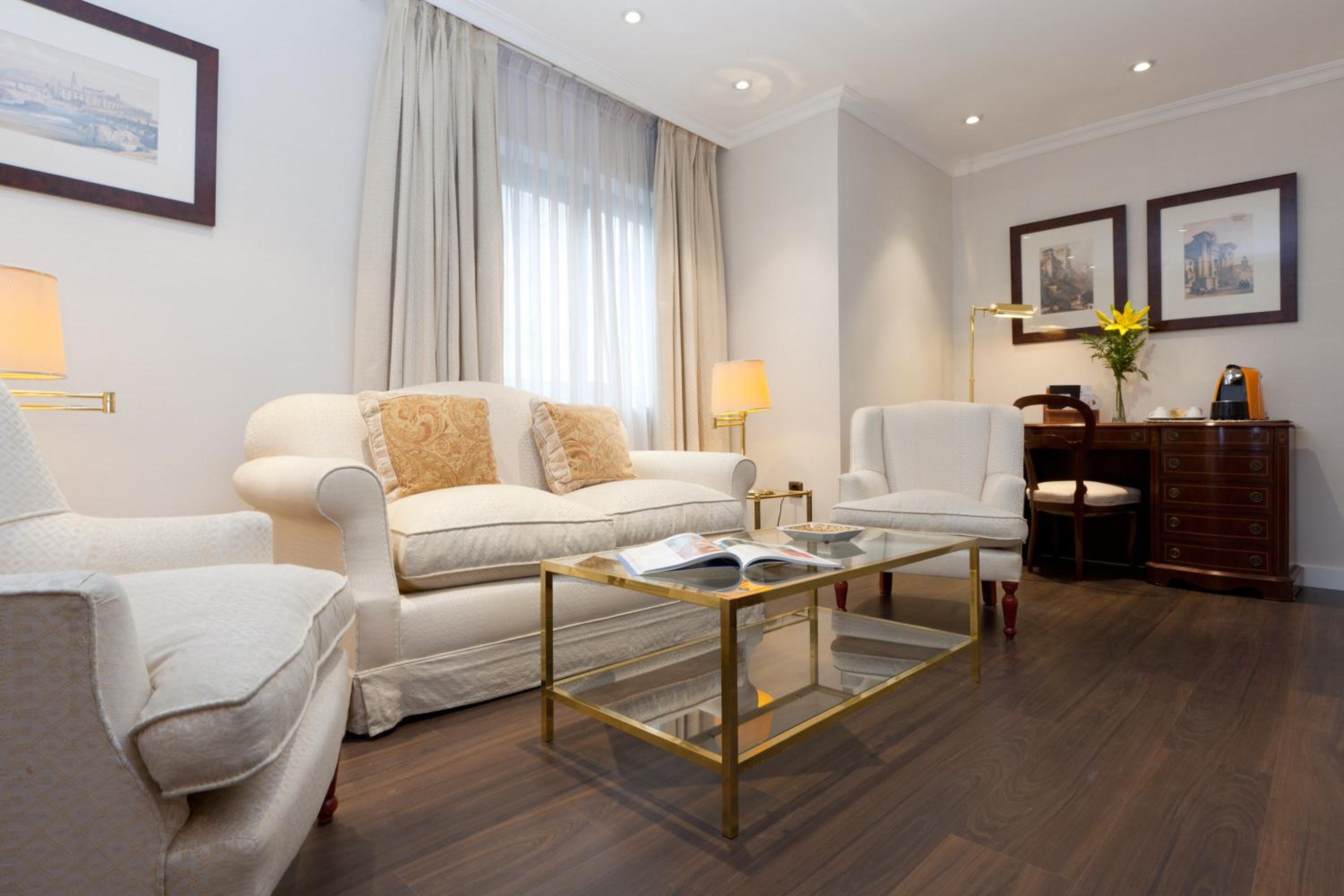 A sitting area with cream armchairs, a fabric sofa, a glass-topped coffee table, and dark wood floors.