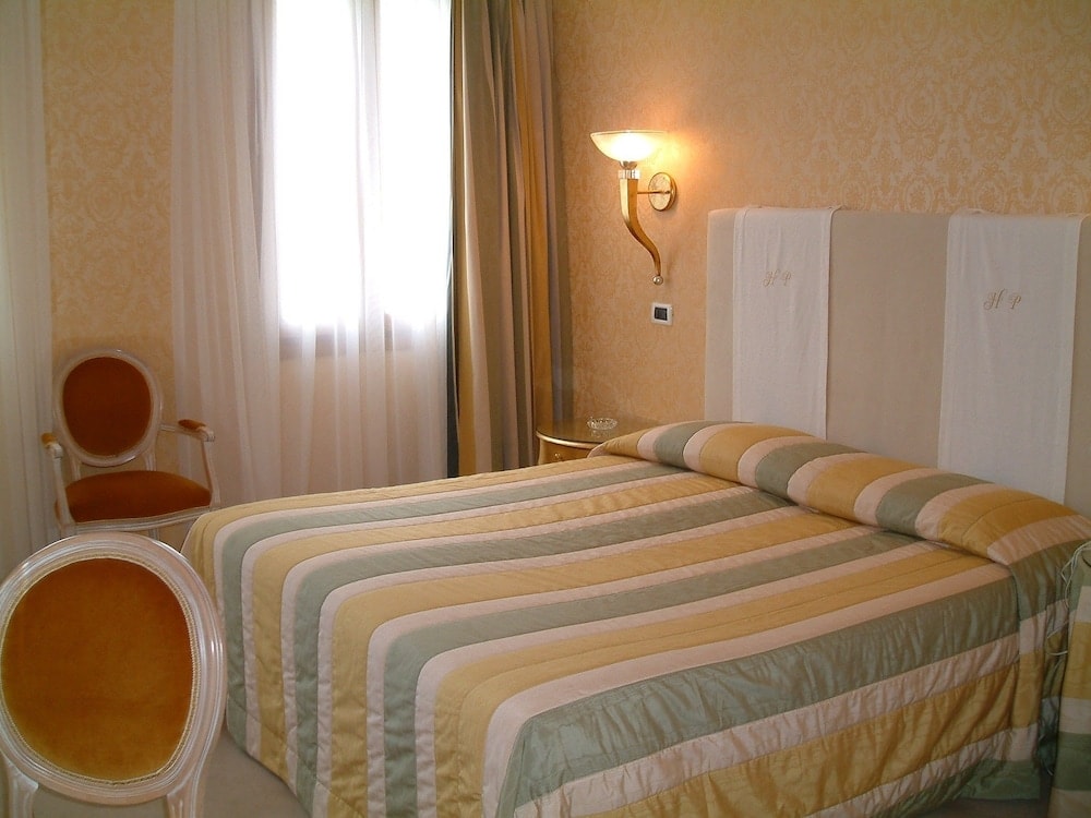 A bedroom features patterned damask wallpaper, a striped bedspread, and plush armchairs.