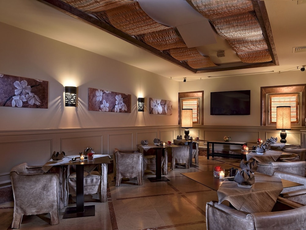 An indoor dining room contains tables with leather armchairs beneath fabric ceiling panels.