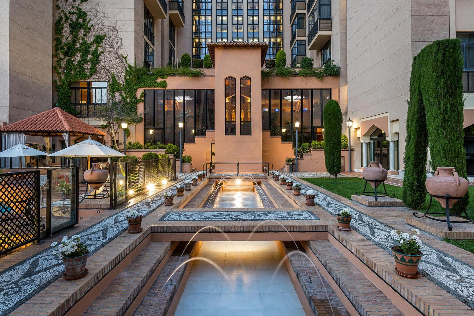 An Andalusian-style courtyard with tiered water fountains, stone mosaics, clay urns, and hotel walls.