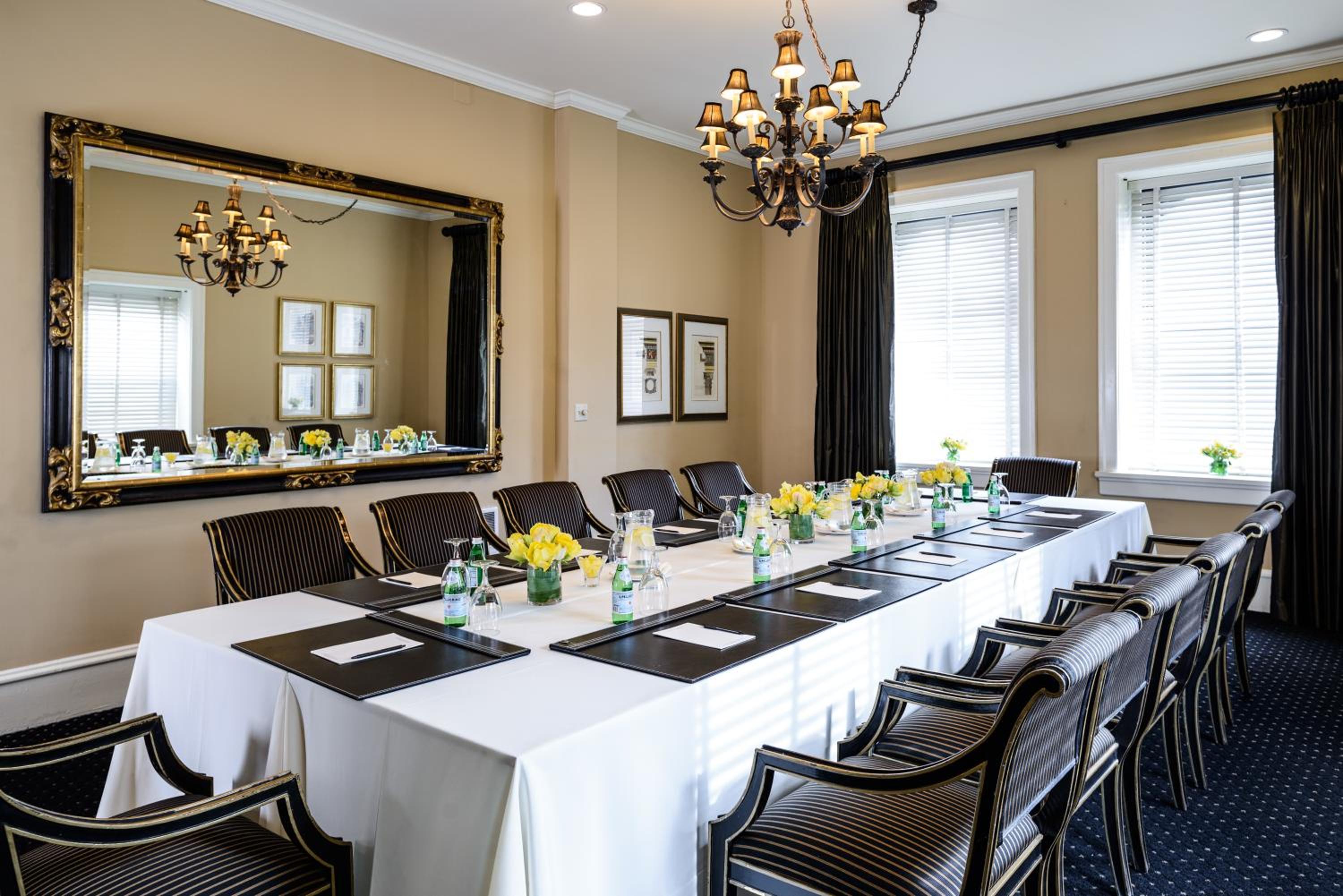 A meeting room table draped in white cloth, flanked by striped armchairs below a chandelier and framed mirror.