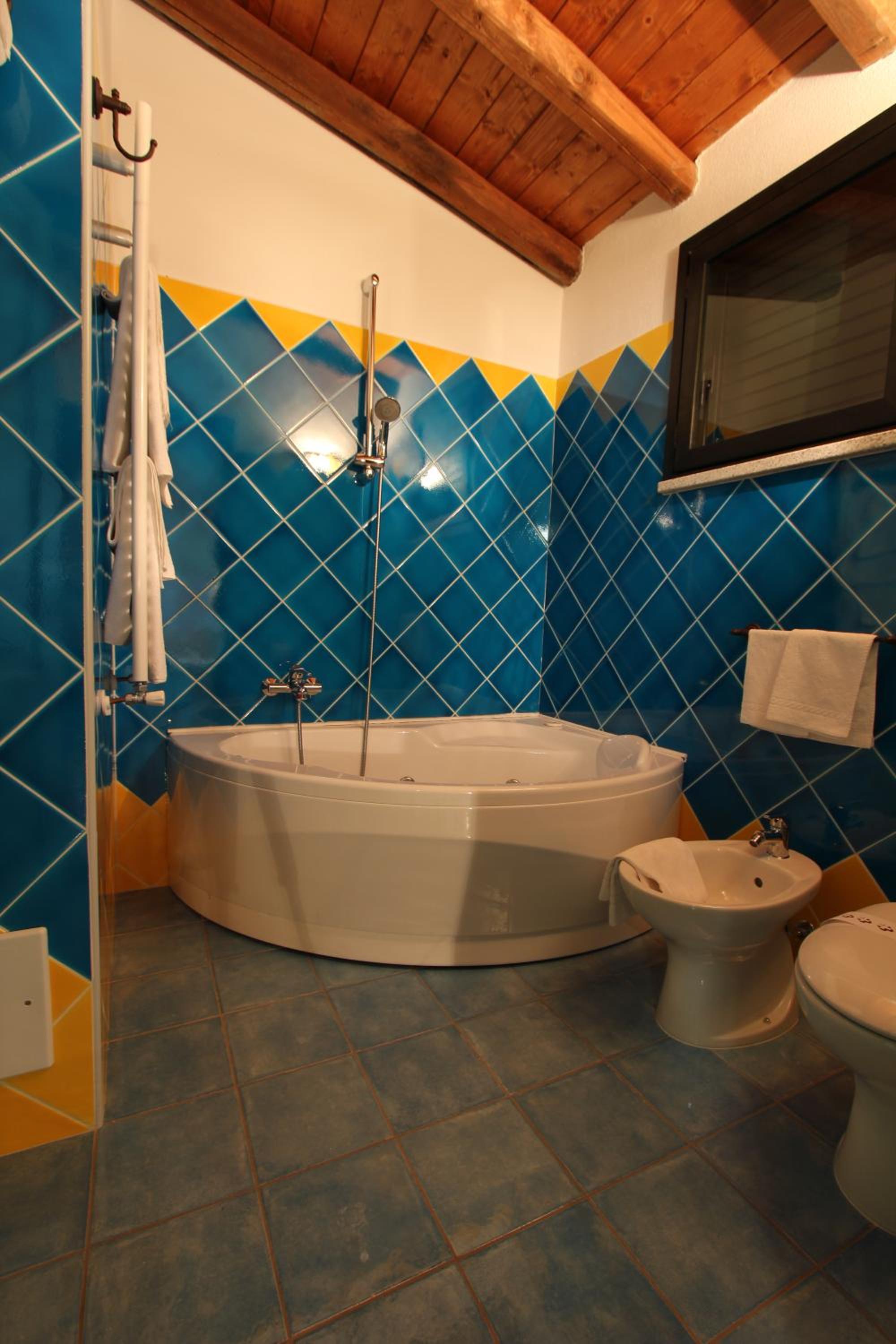 Bathroom with blue and yellow wall tiles, a corner soaking tub, and an exposed wooden beam ceiling.