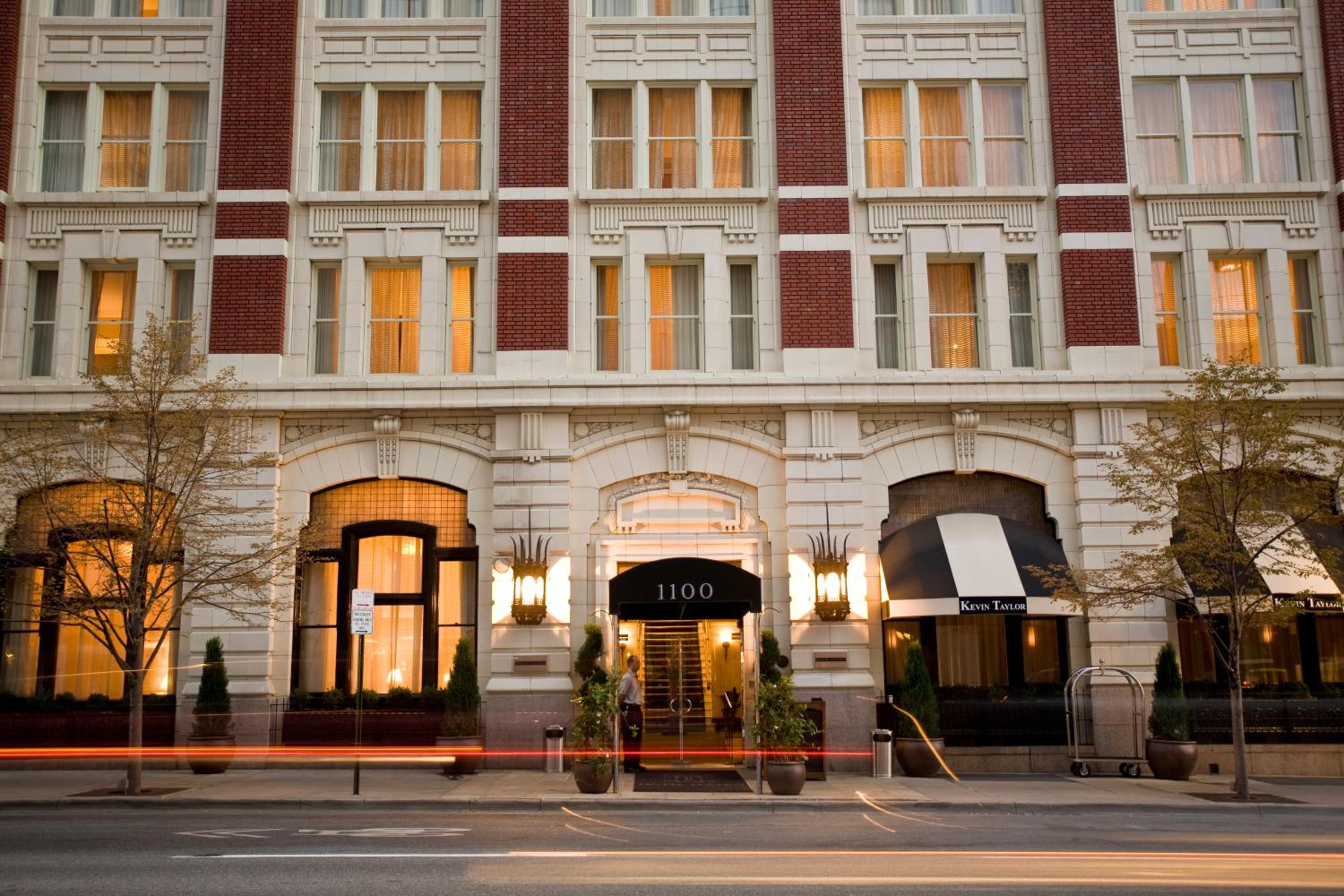Exterior stone and brick facade of Hotel Teatro illuminated at dusk with ornate lanterns beside the entrance.