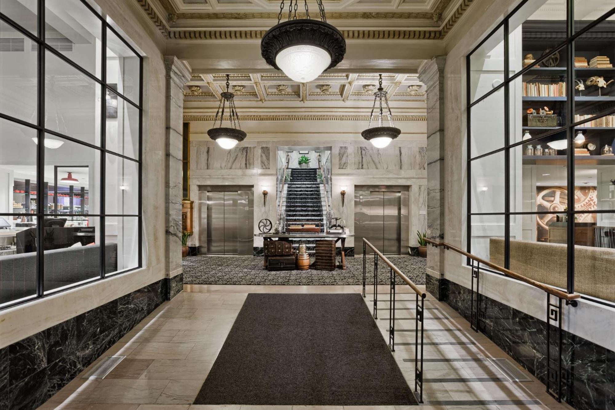 A marble lobby hallway with coffered ceilings, dark hanging pendant lights, and a central staircase.