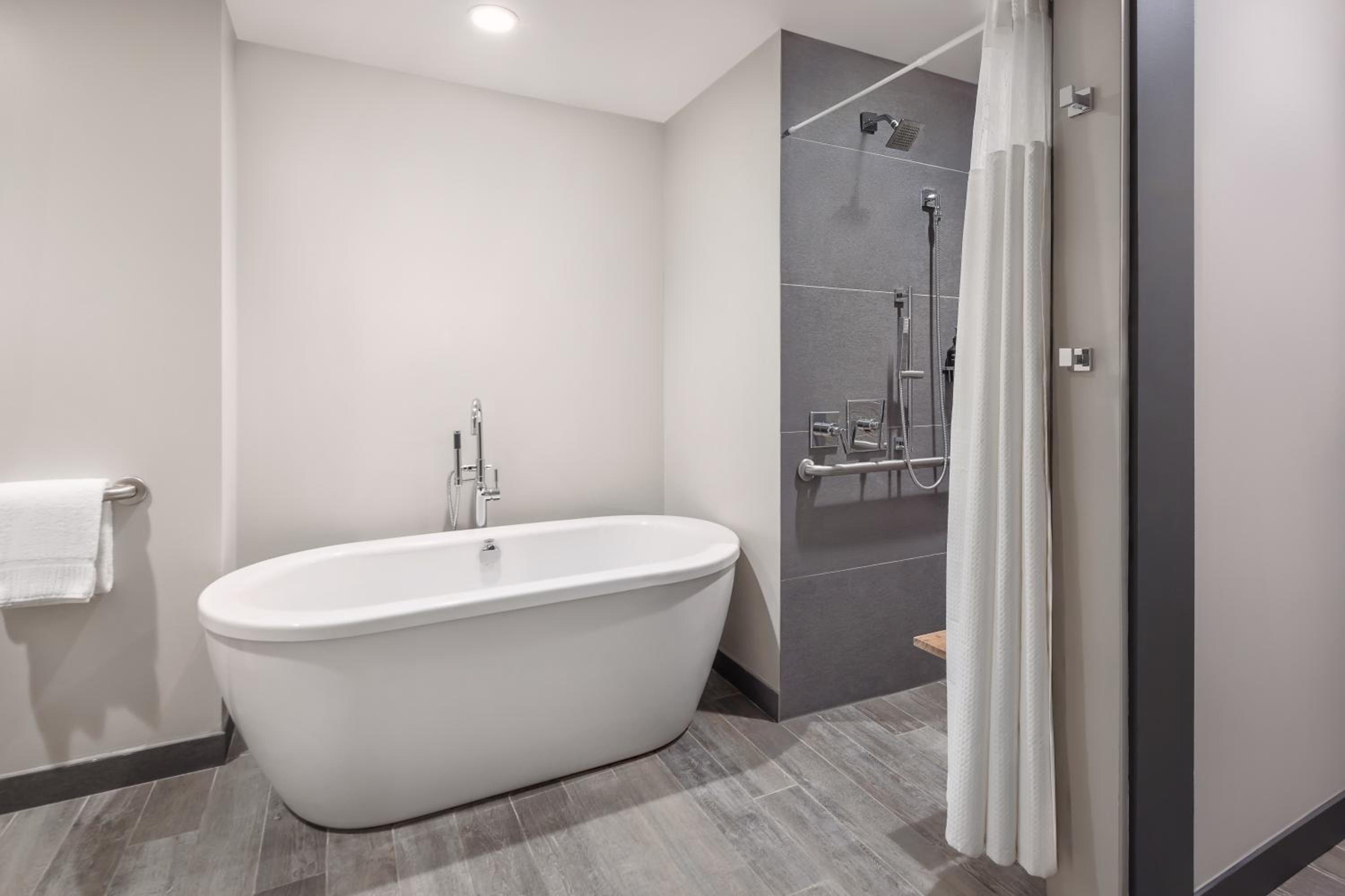 A bathroom with a white freestanding soaking tub beside an open shower lined in gray tile.