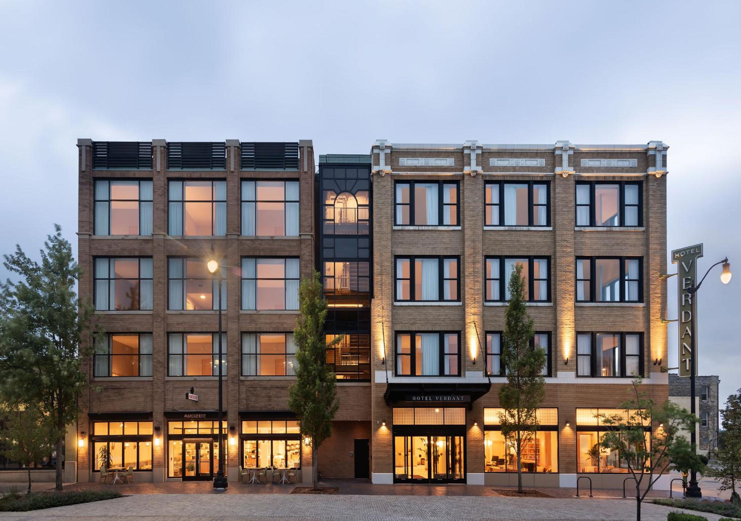 Brick exterior of Hotel Verdant at dusk with glowing windows and illuminated street-level entrances.