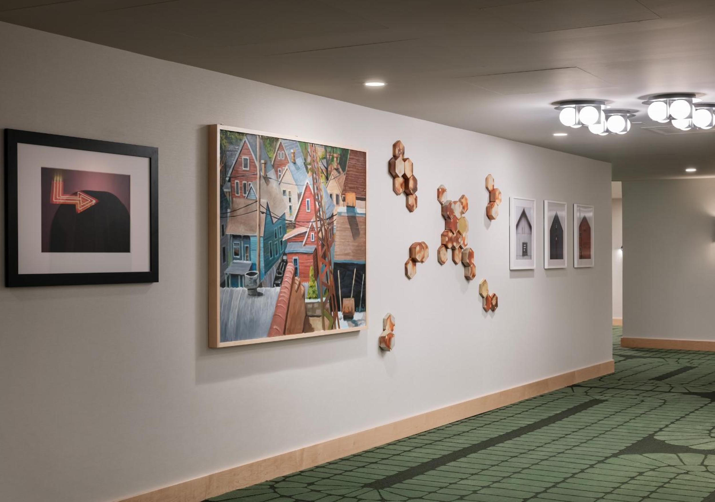 A hotel hallway featuring patterned green carpeting and framed artwork along white walls.