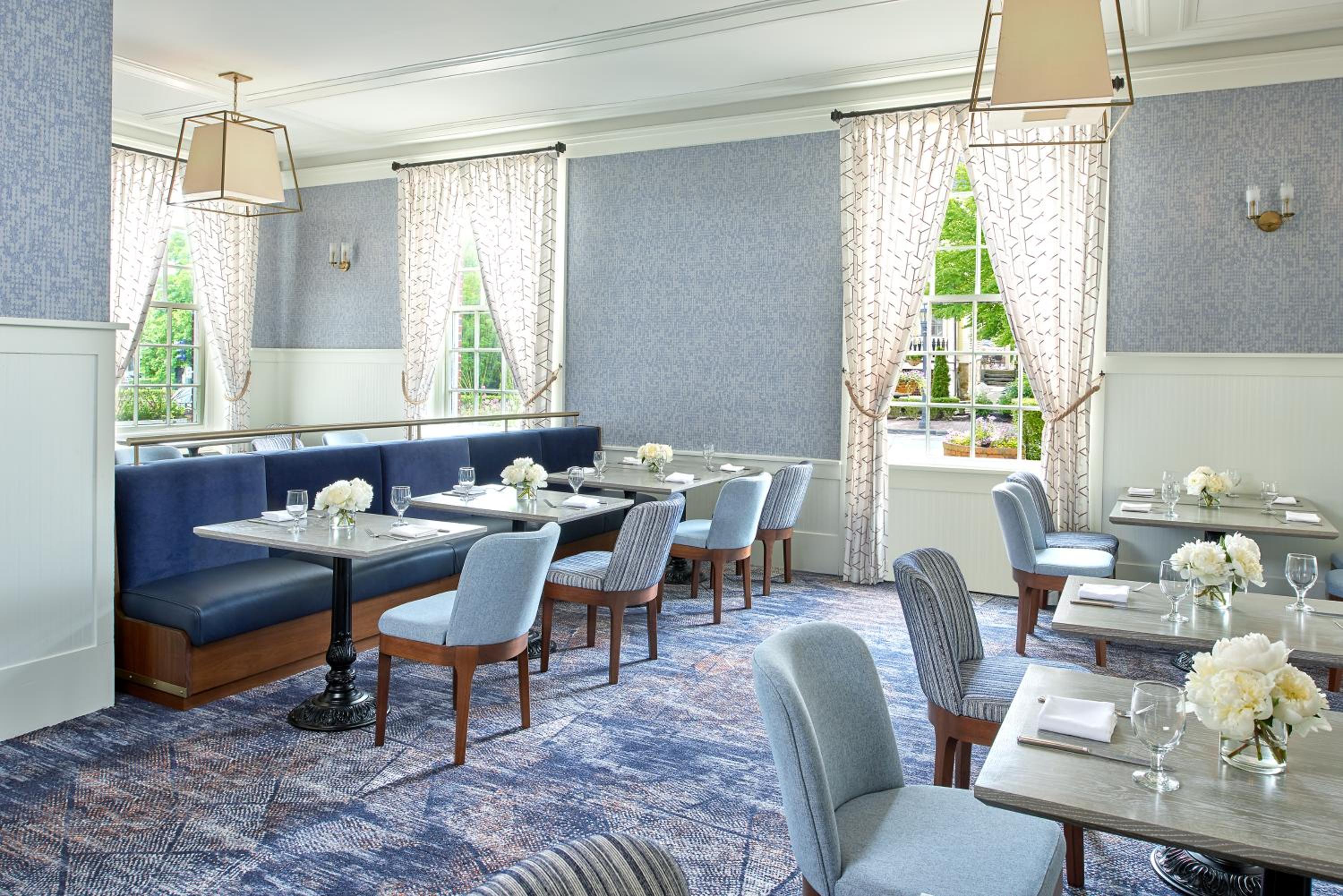 A restaurant dining room with blue wallpaper, patterned carpet, banquette seating, and set dining tables.