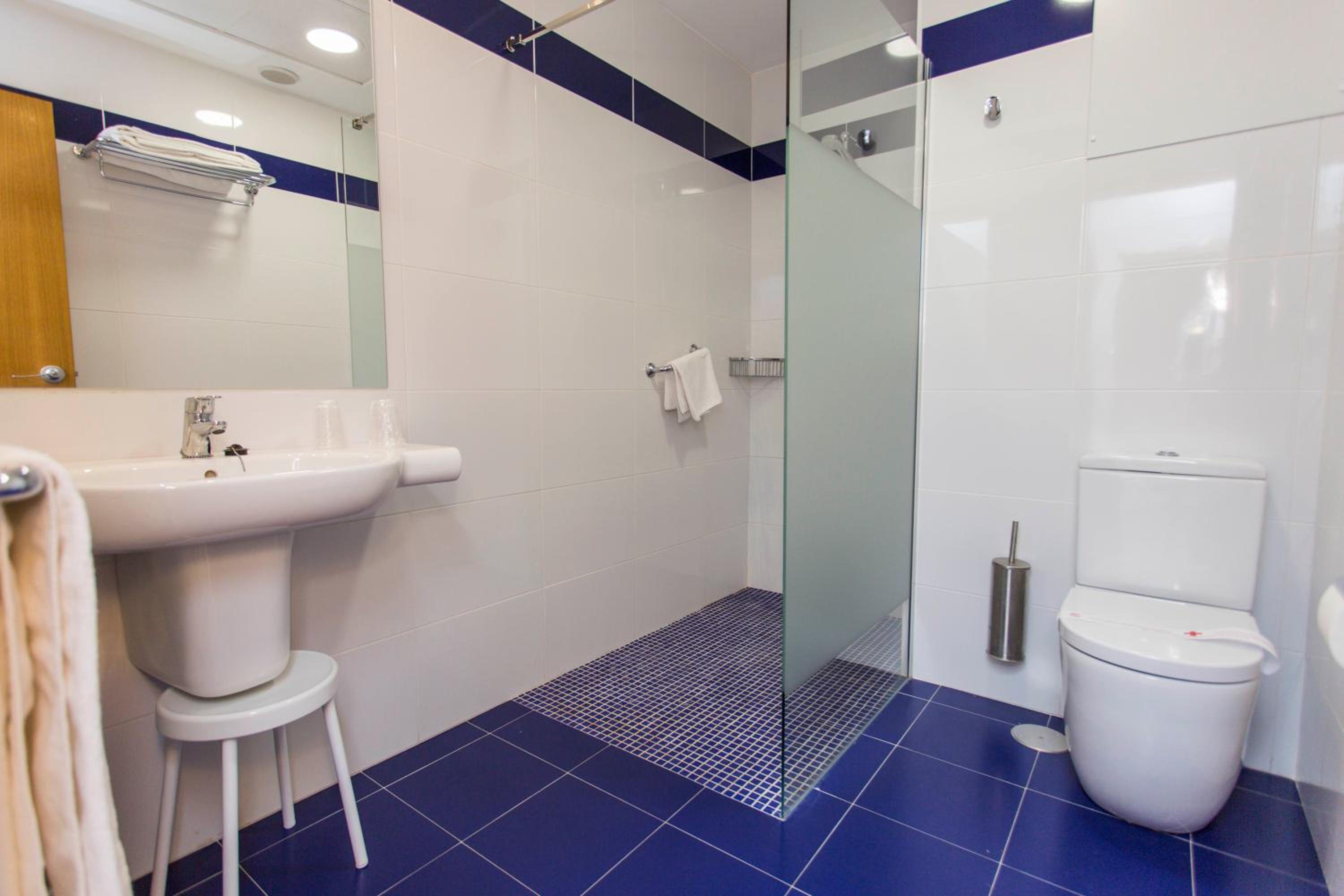 Bathroom with blue floor tiles, white tiled walls, a walk-in glass shower, and white fixtures.