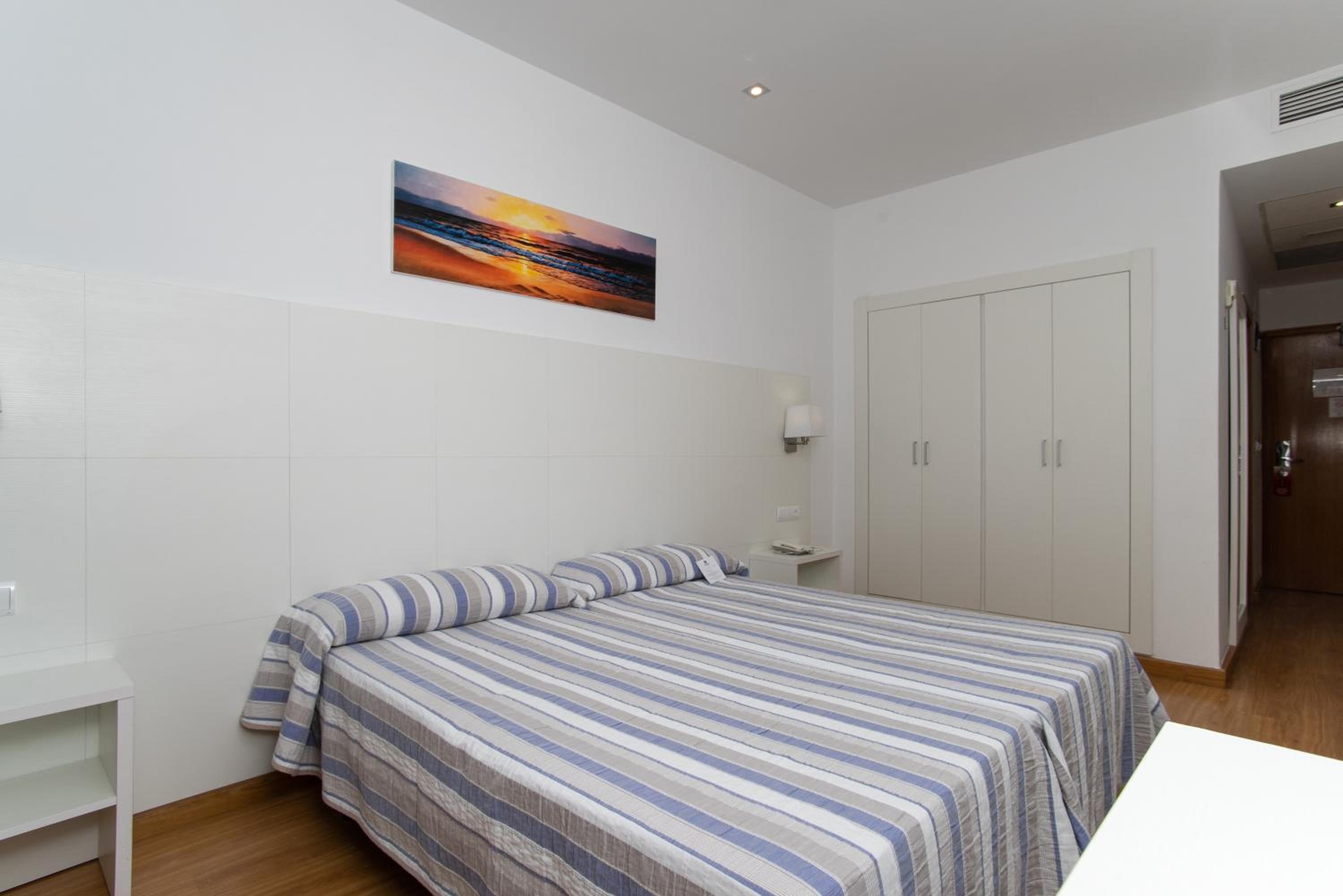 Bedroom featuring striped bedding, a beach sunset picture on the wall, and built-in white wardrobes.