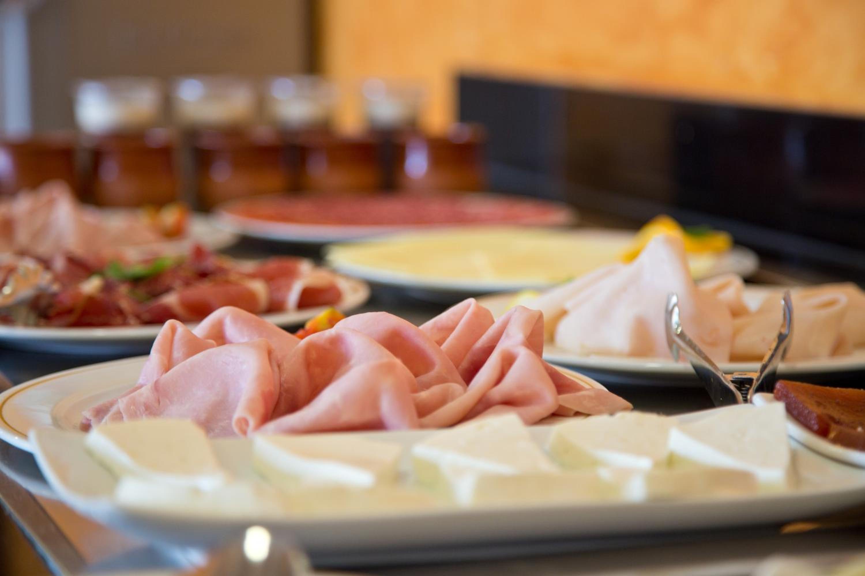 Slices of folded ham and white cheese arranged on buffet platters with serving tongs.