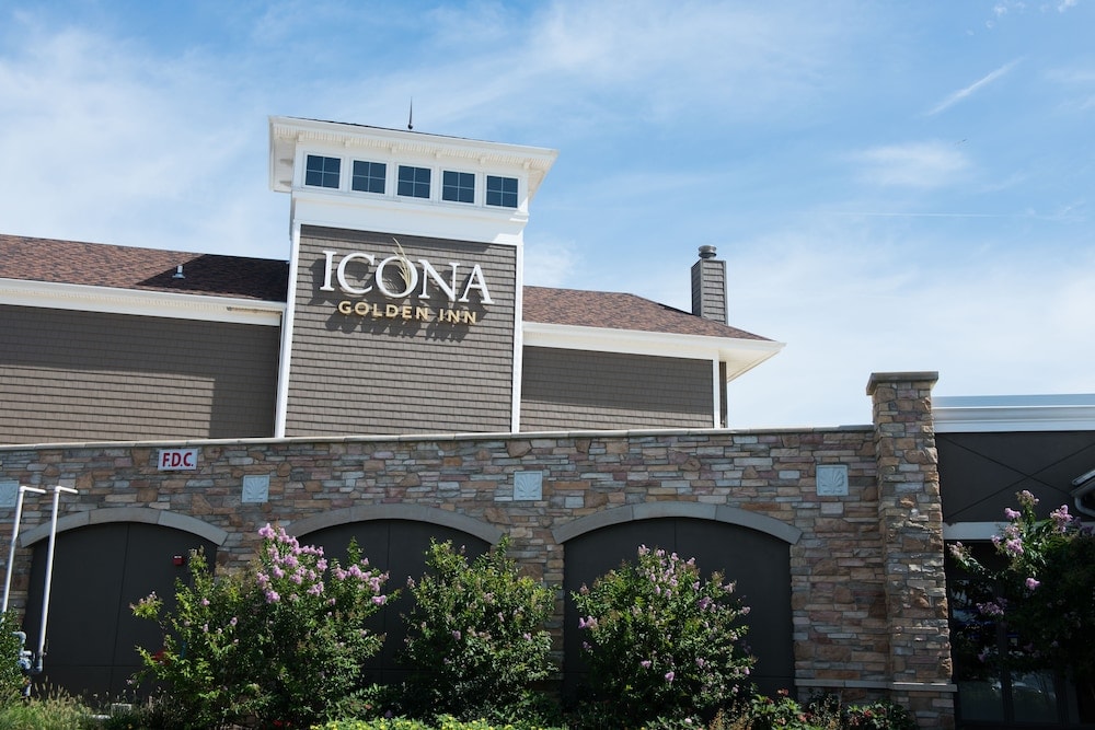 Exterior facade of ICONA Avalon with wood shingles, stone arches along the lower wall, and flowering bushes.
