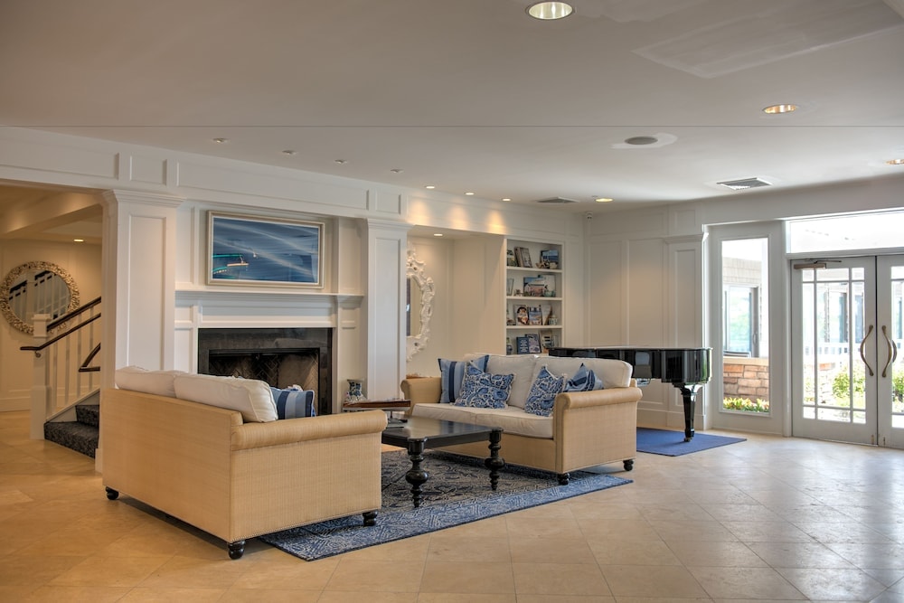 Lobby lounge with beige sofas around a dark coffee table, fireplace flanked by white columns, and a grand piano.
