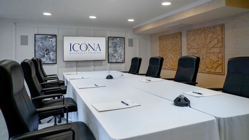 Conference room centered on a long white-draped table with black leather executive chairs and a wall-mounted screen.