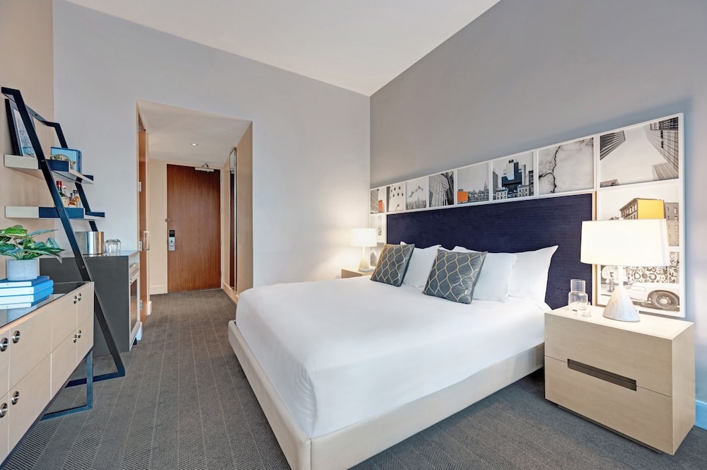 A hotel bedroom with a white-dressed bed, navy headboard lined with photographs, and wood nightstands.