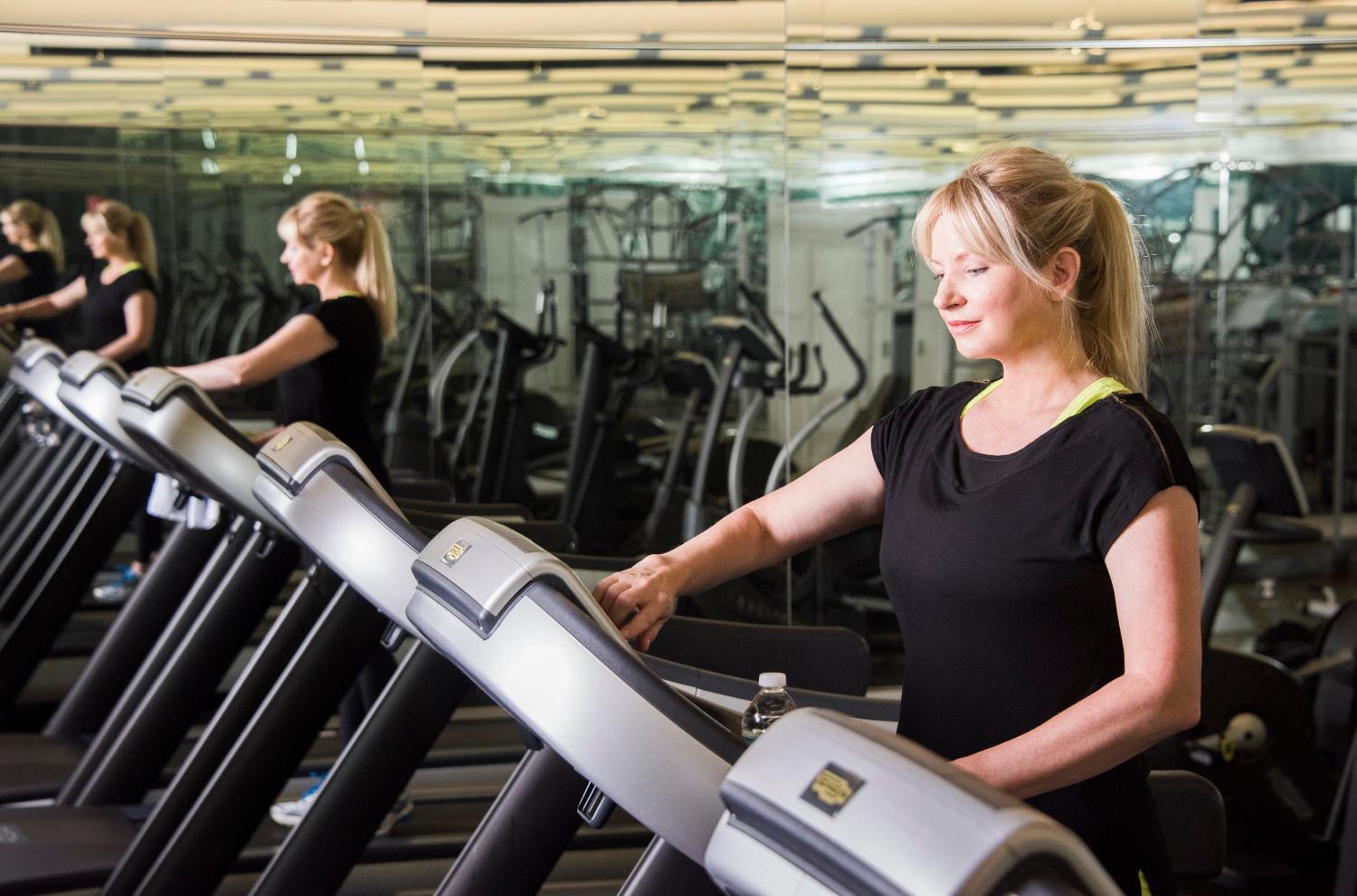 A woman in athletic wear exercises on a treadmill in a fitness studio lined with mirrors.