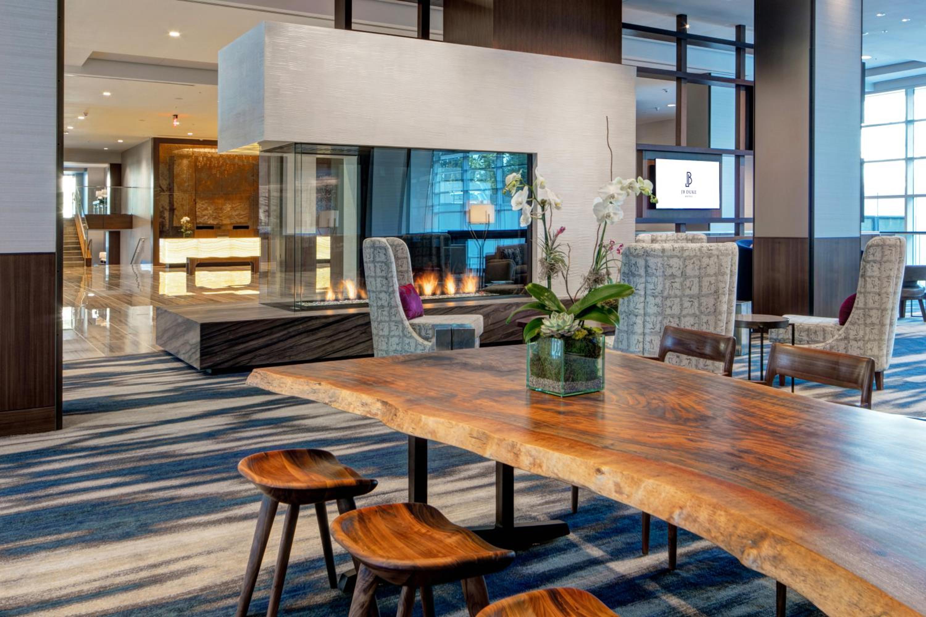 A hotel lounge with a live-edge wood table, sculpted wooden stools, and a see-through glass fireplace.