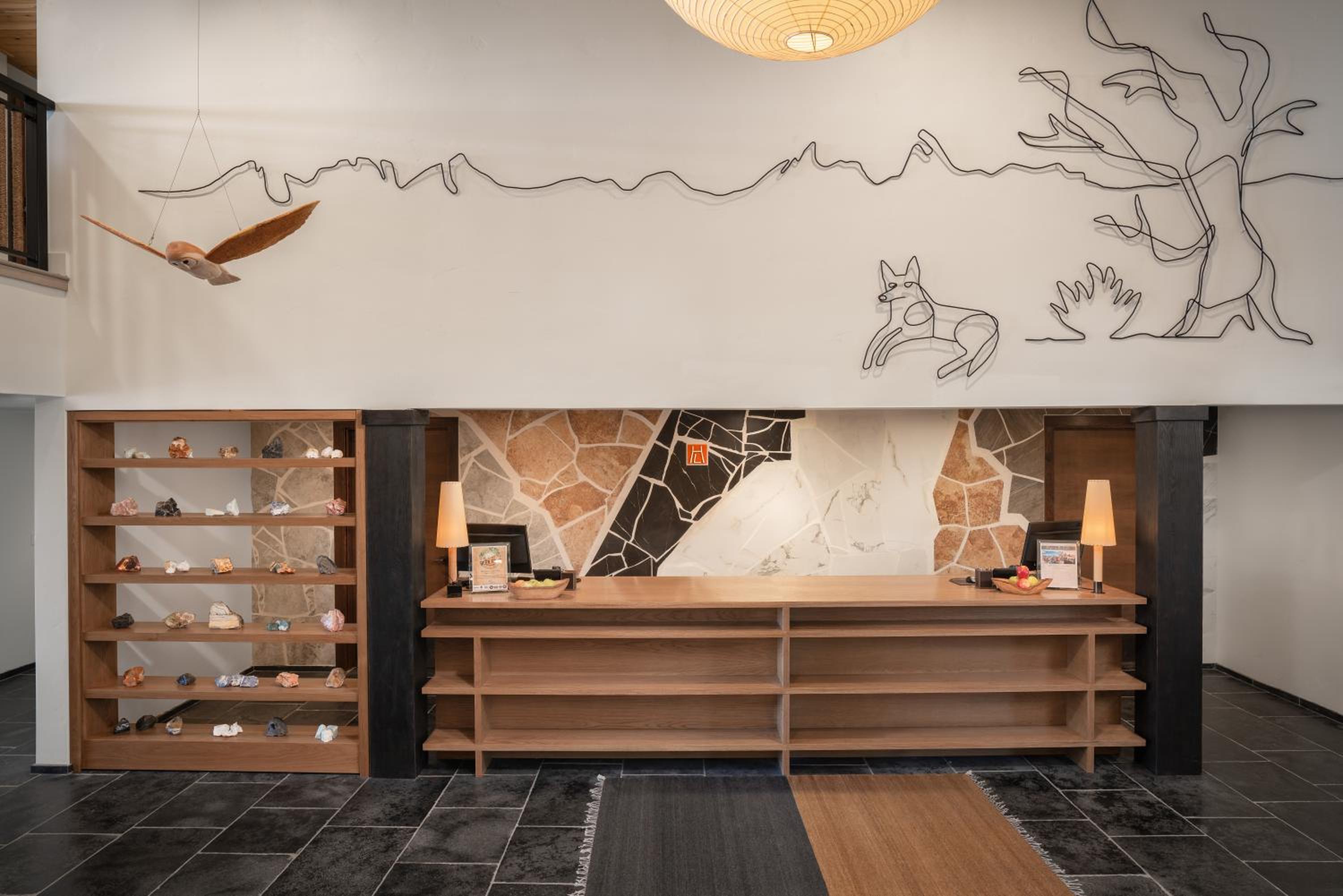 Wooden reception counter below a wall featuring wire contour art of a landscape, a bird, and a coyote.