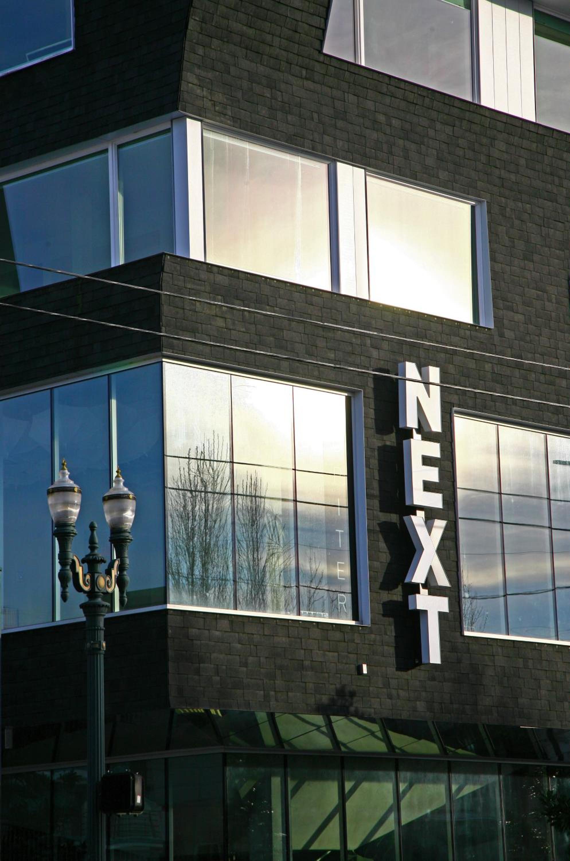 Exterior facade of Jupiter NEXT with dark shingles, large glass windows, and a vertical white sign reading NEXT.