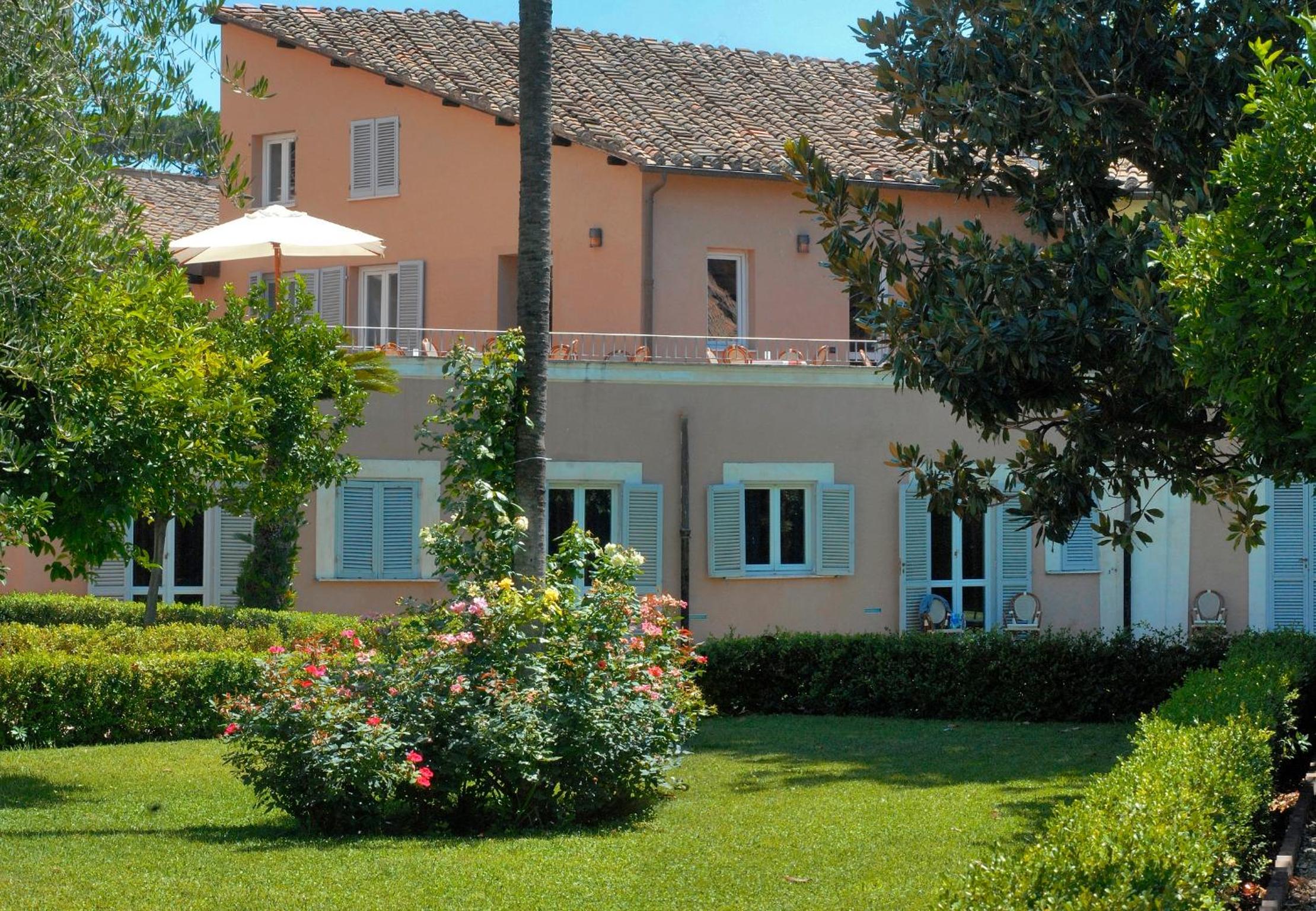 Peach-colored facade of Kolbe Hotel Rome with shutters, viewed across a lawn with rose bushes.