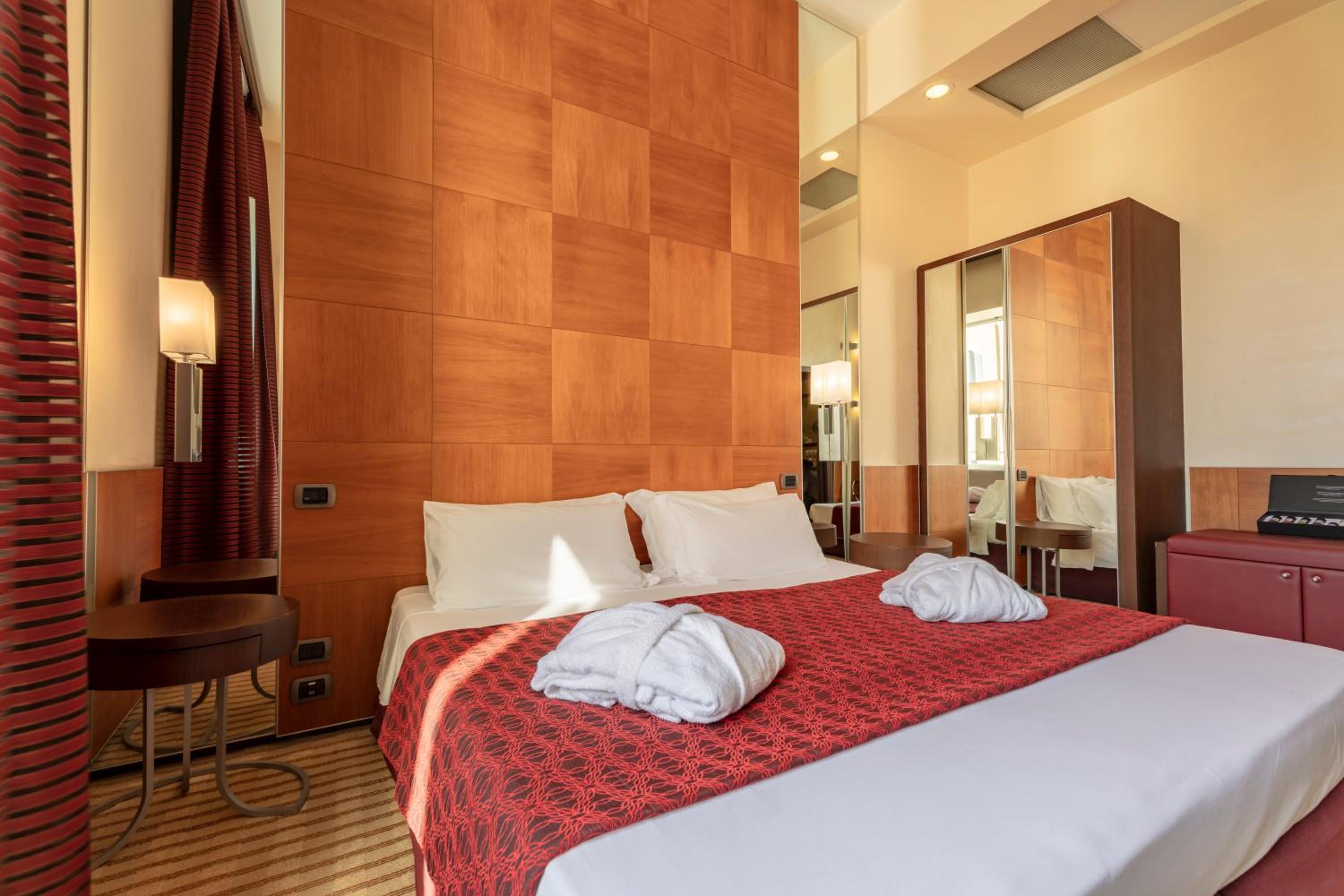 Guest bedroom with a wood-paneled wall, bed with red patterned runner, and mirrored wardrobe.