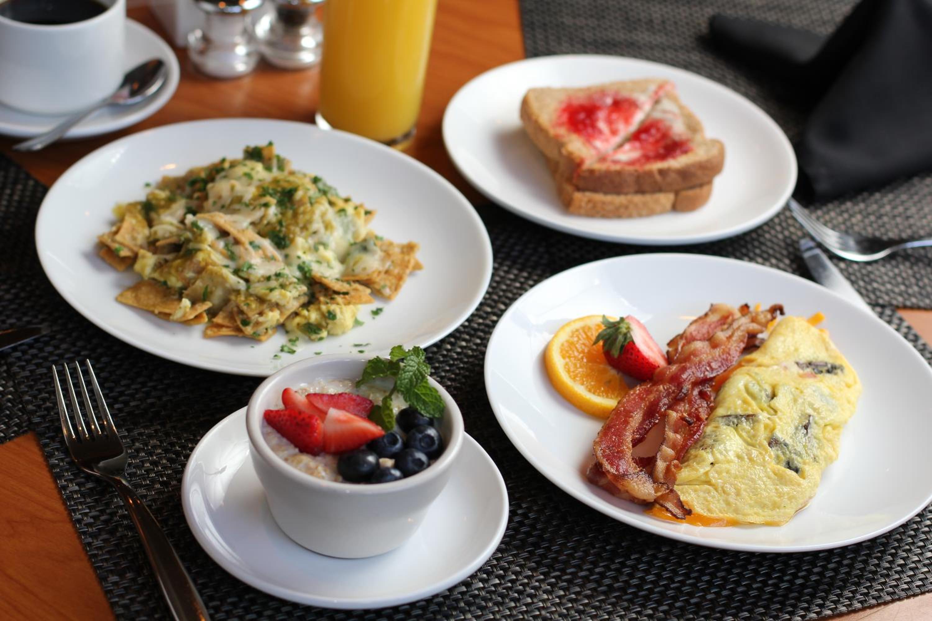 A breakfast spread of chilaquiles, an omelet with bacon, jam-topped toast, and oatmeal with fresh berries.