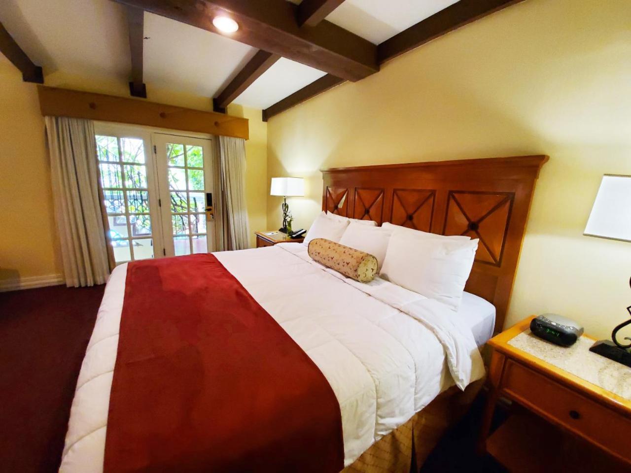 A bedroom with exposed ceiling beams, a bed dressed in white with a red runner, and glass doors to a patio.