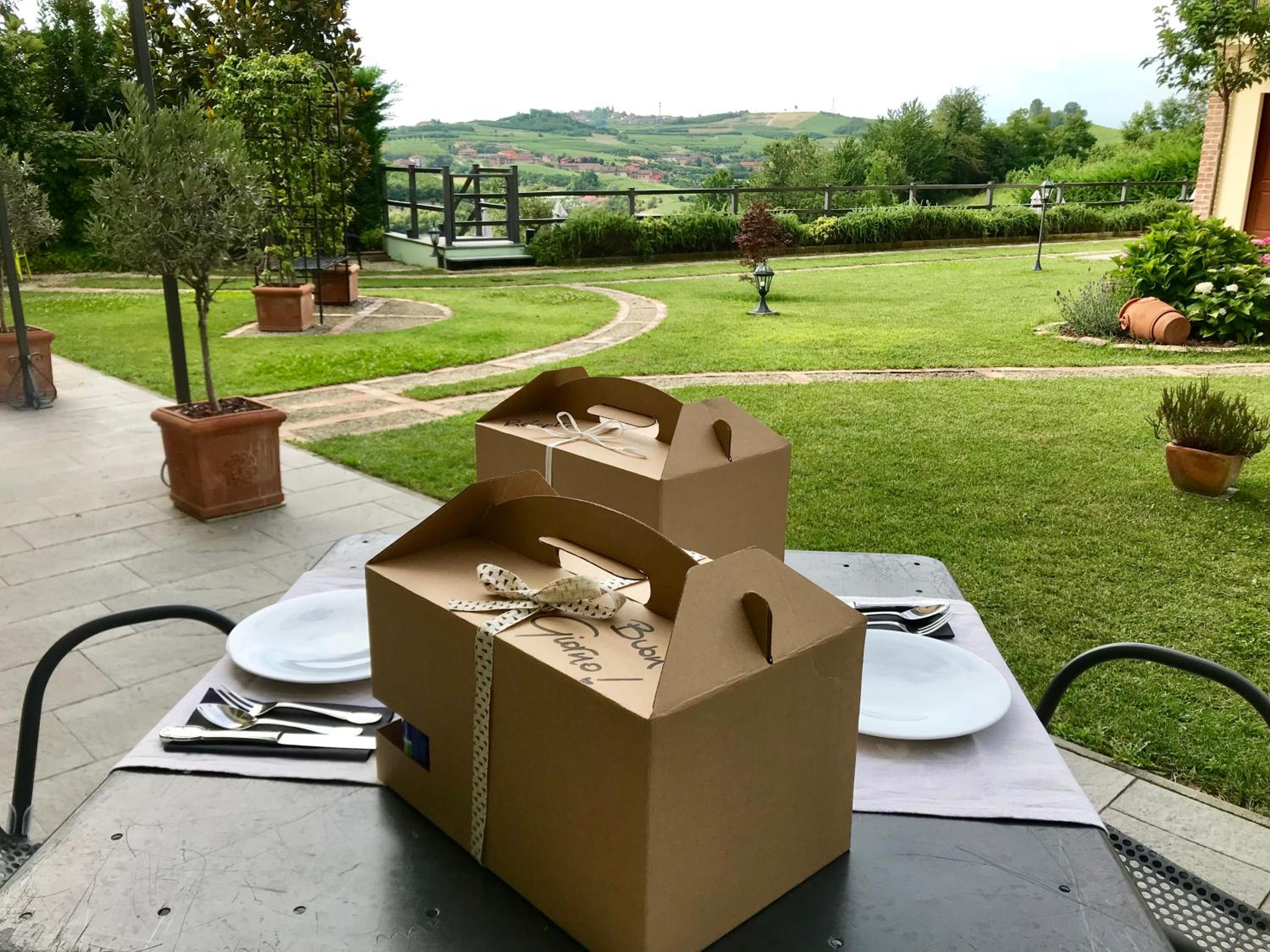 Picnic meal boxes and plates set on a patio table overlooking a green lawn and rolling hills.