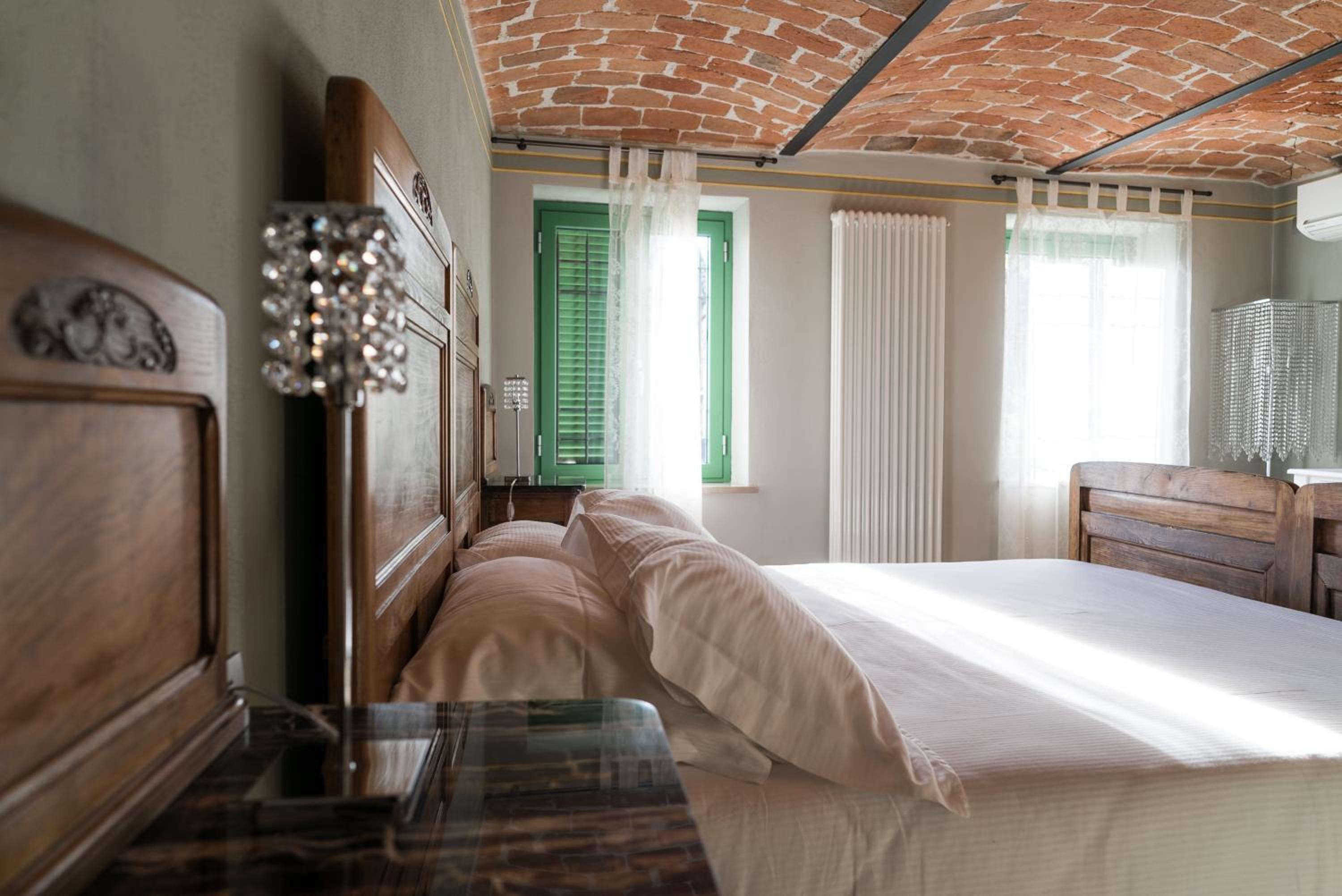 A bedroom with an arched brick ceiling, wooden bed, white linens, and a window with green shutters.